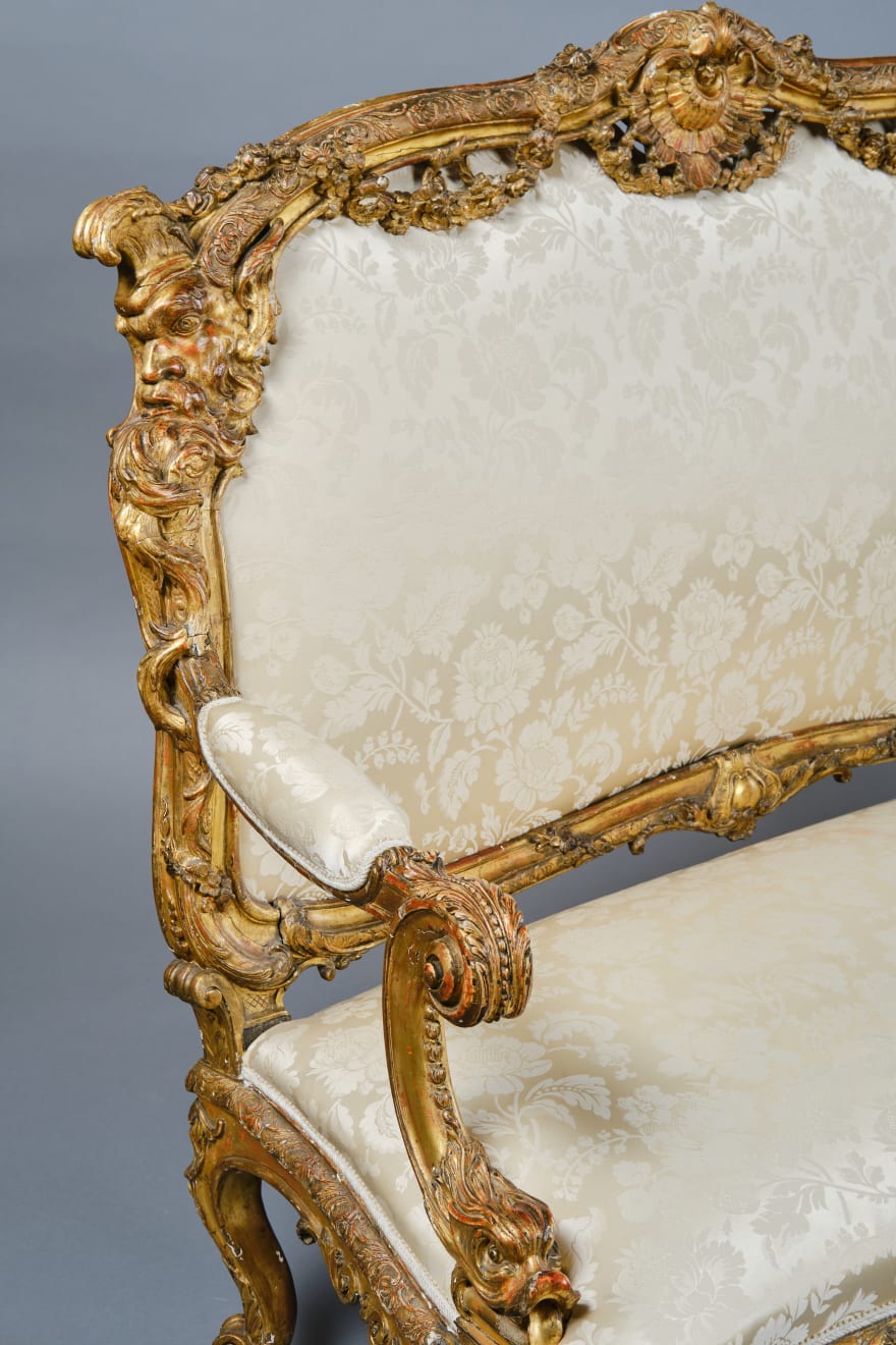 CARVED AND GILDED WOOD SOFA, FRANCE, 18th CENTURY, two-seater, mixtilinear layout and entirely traversed by relief carvings, with floral festoons, garlands, manly masks in the back uprights and stylized dolphins in the armrests with curly finials, upholstered in modern fabric with classical decoration, the back removable