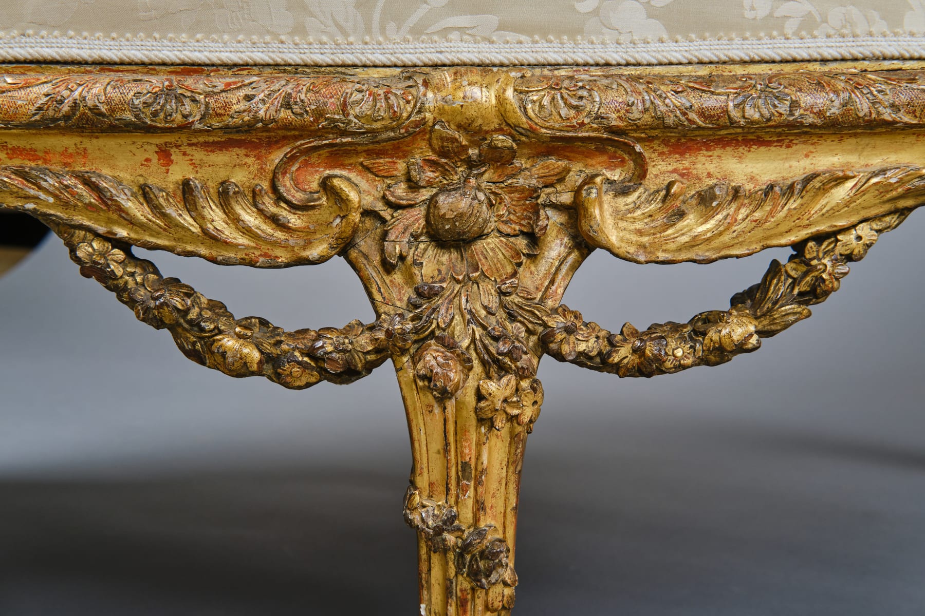 CARVED AND GILDED WOOD SOFA, FRANCE, 18th CENTURY, two-seater, mixtilinear layout and entirely traversed by relief carvings, with floral festoons, garlands, manly masks in the back uprights and stylized dolphins in the armrests with curly finials, upholstered in modern fabric with classical decoration, the back removable