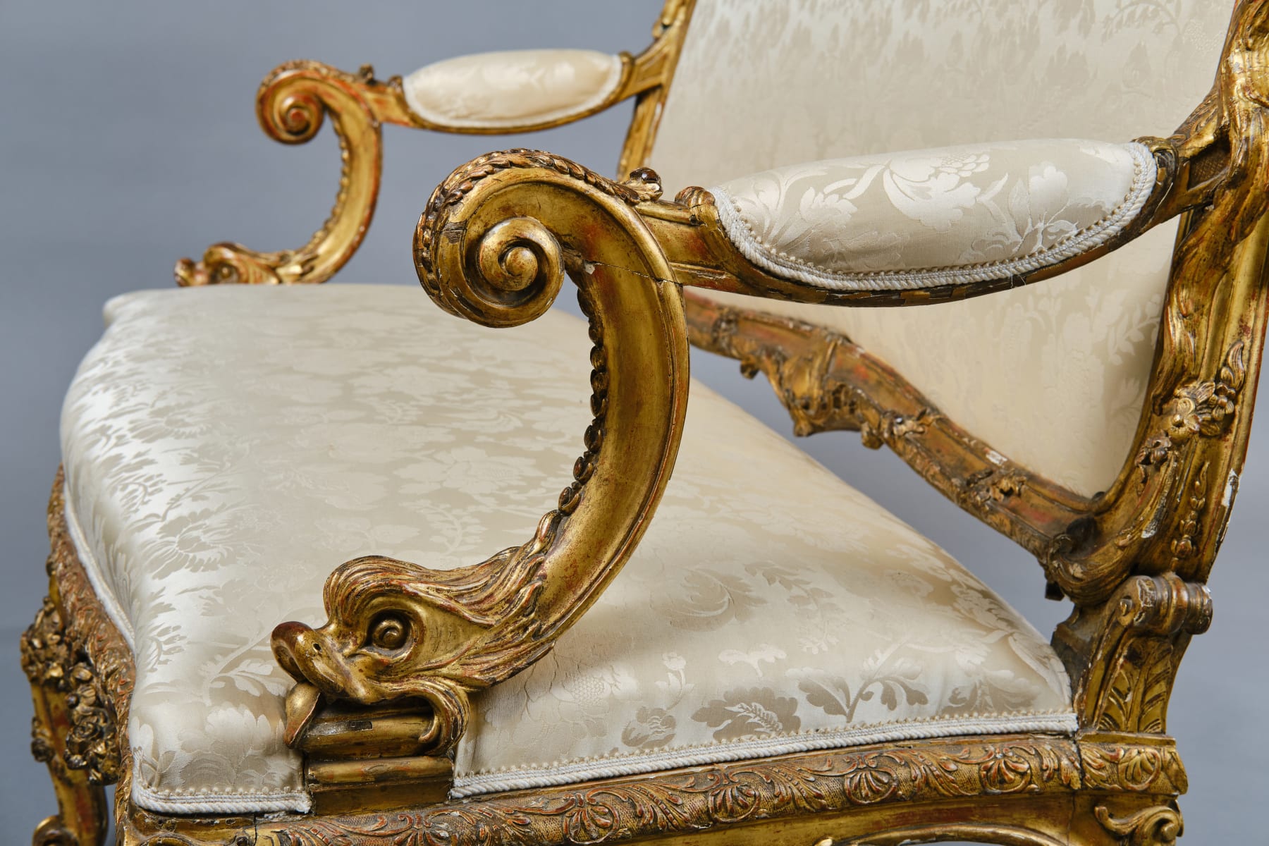 CARVED AND GILDED WOOD SOFA, FRANCE, 18th CENTURY, two-seater, mixtilinear layout and entirely traversed by relief carvings, with floral festoons, garlands, manly masks in the back uprights and stylized dolphins in the armrests with curly finials, upholstered in modern fabric with classical decoration, the back removable