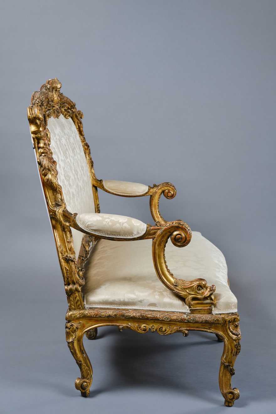 CARVED AND GILDED WOOD SOFA, FRANCE, 18th CENTURY, two-seater, mixtilinear layout and entirely traversed by relief carvings, with floral festoons, garlands, manly masks in the back uprights and stylized dolphins in the armrests with curly finials, upholstered in modern fabric with classical decoration, the back removable