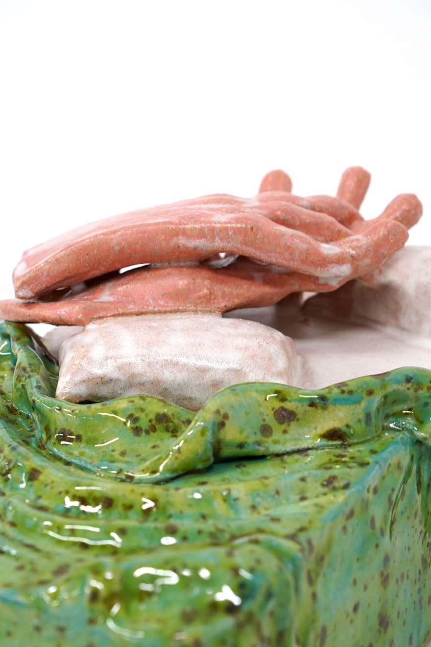 ceramic sculpture of a hand laying in a bed