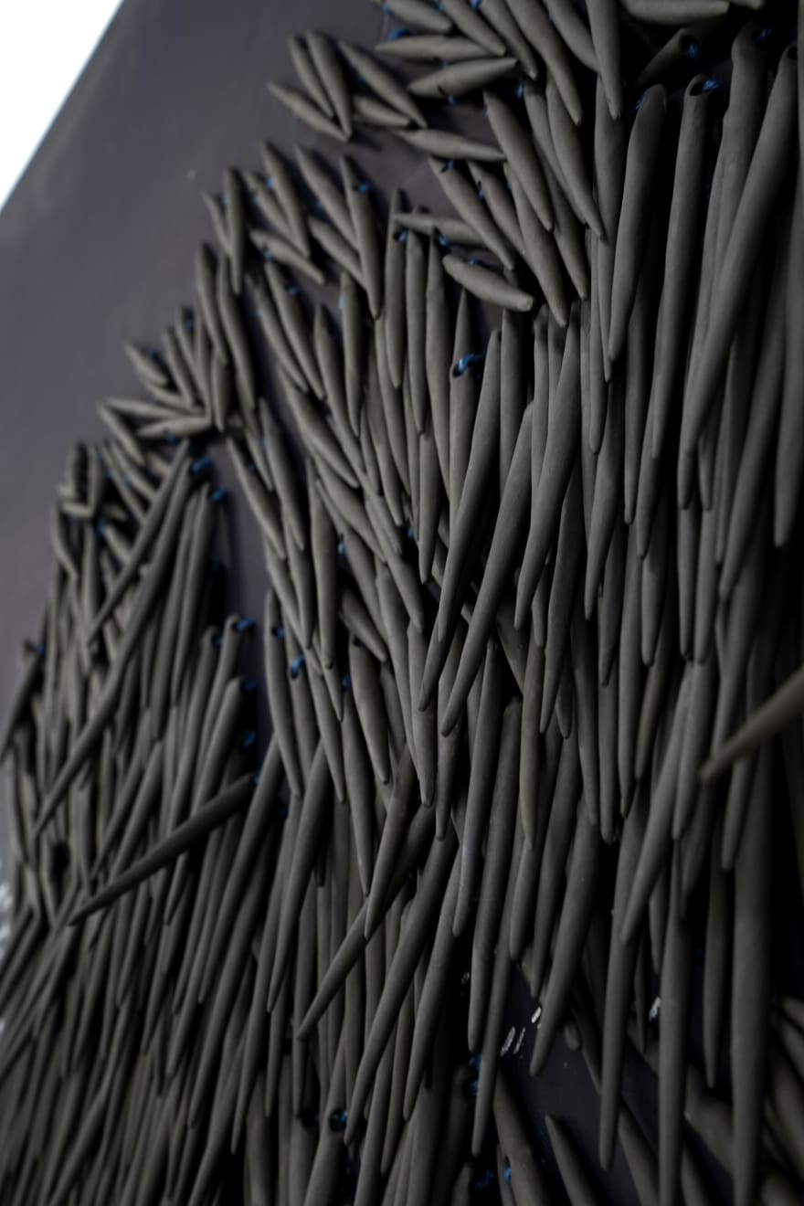 small ceramic needles sewn to a dark indigo canvas