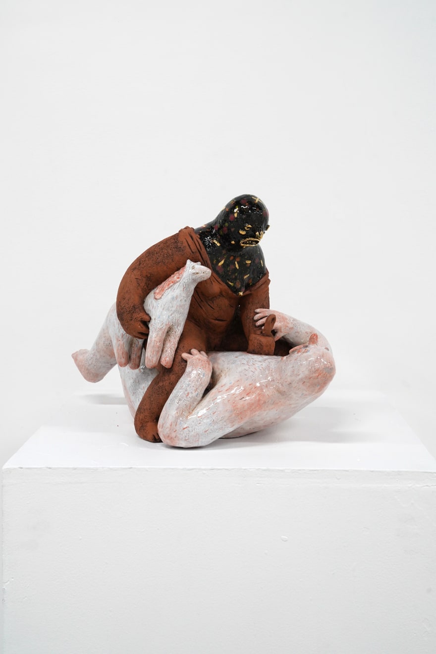 ceramic sculpture of a being sitting on top and stabbing another being