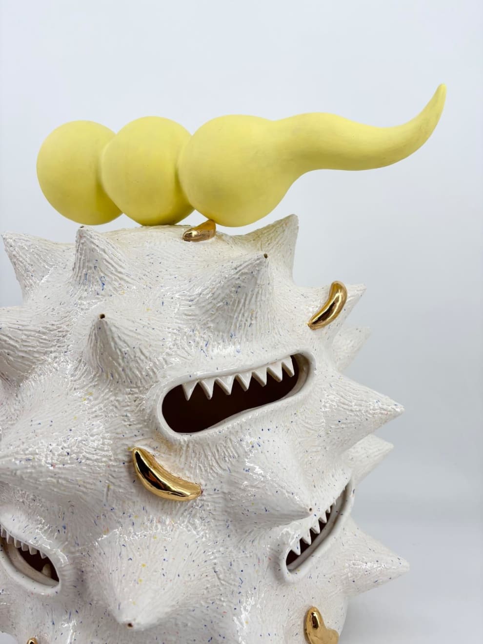 Detail of “Fat white spooter” by Kartini Thomas, showing yellow horned form atop with gold luster and sharp-toothed mouths.