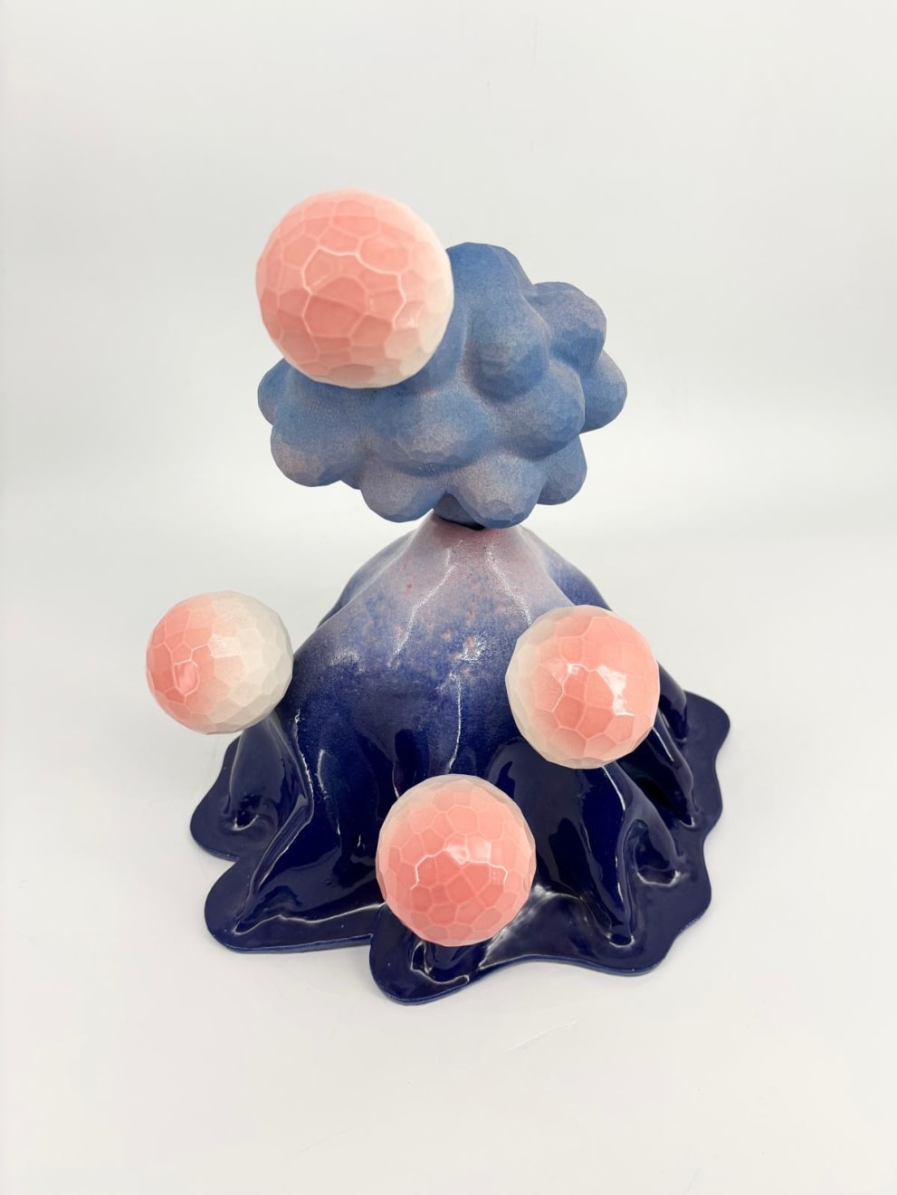 Front view of a ceramic volcano sculpture by Kartini Thomas featuring glossy deep blue glaze and pastel pink faceted spheres.