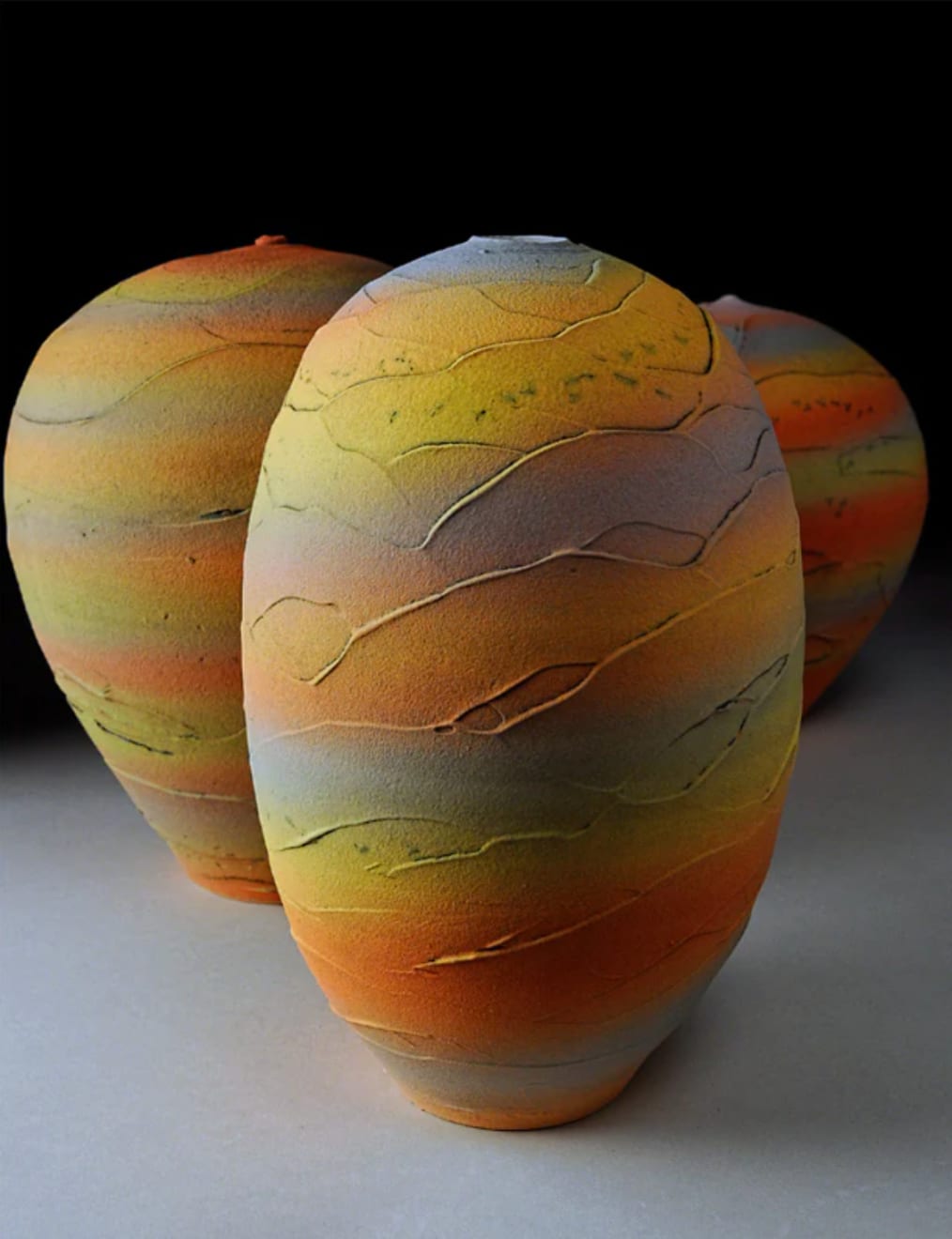 tall earthenware vessel with sunset bands of color with two other vessels in the background by potter Nicholas Bernard
