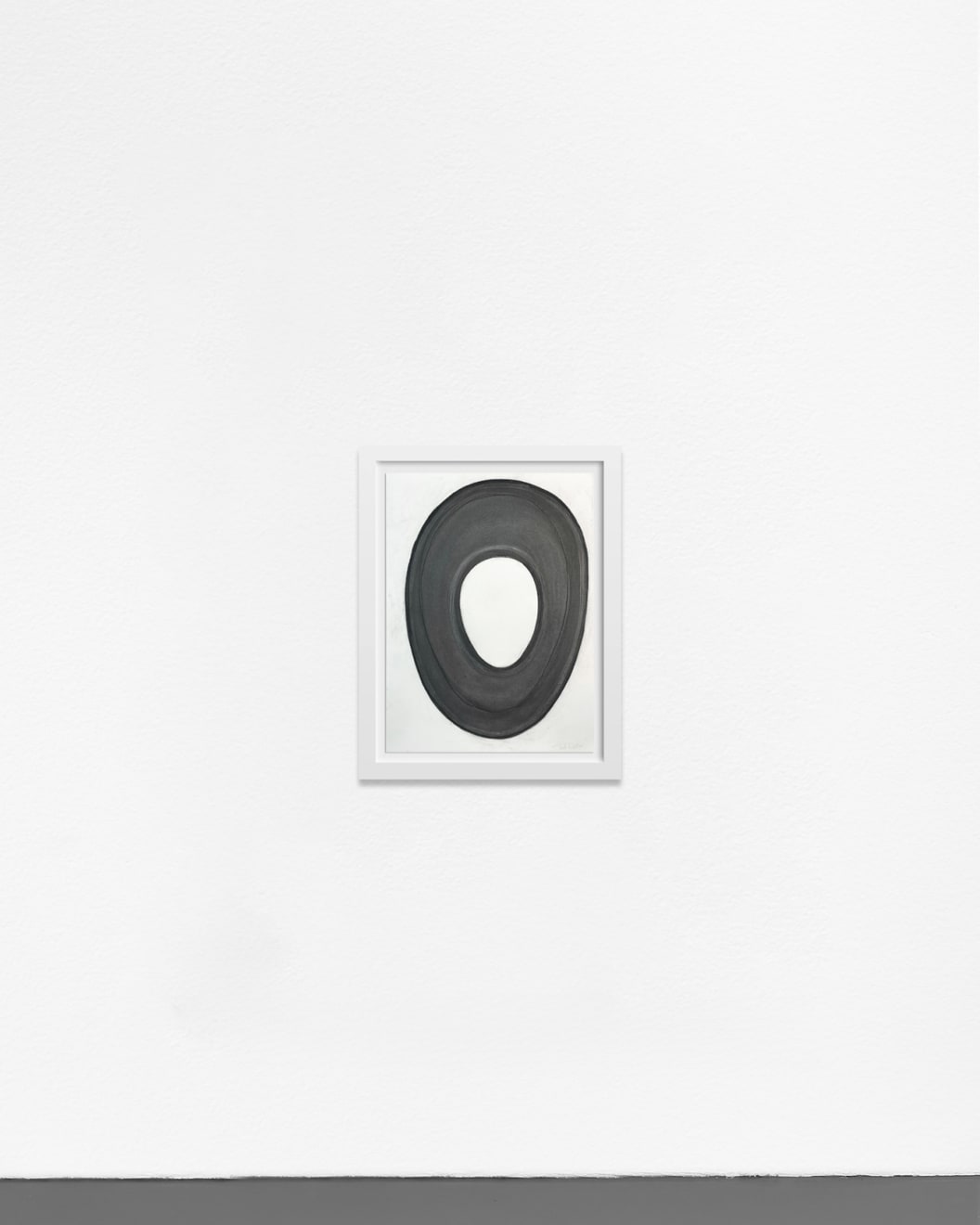 Ted Collier work on paper with a black circle on white background in charcoal framed in white frame hanging on a white wall