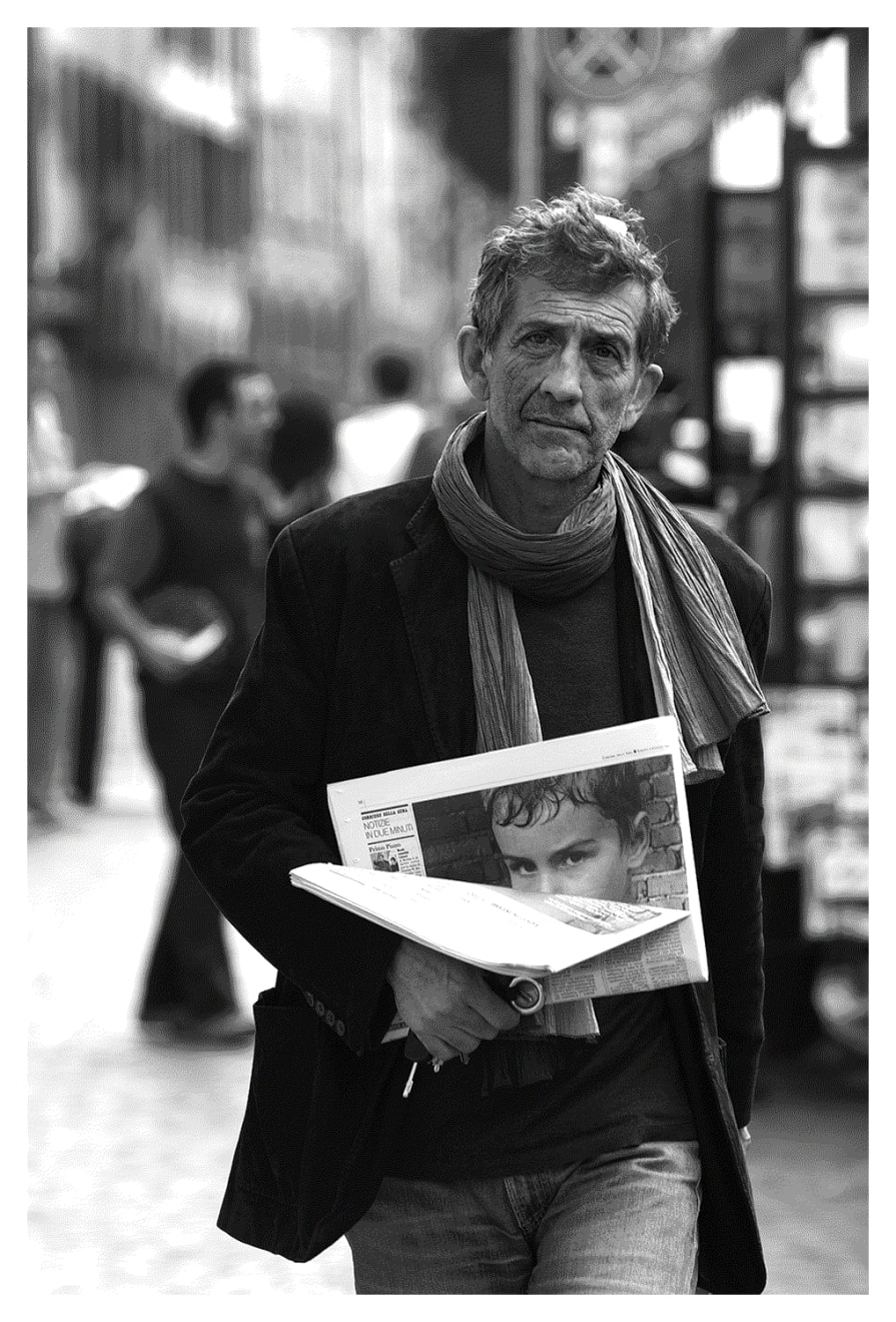 Black and white photograph of a man walking with newspaper in Bologna Italy.