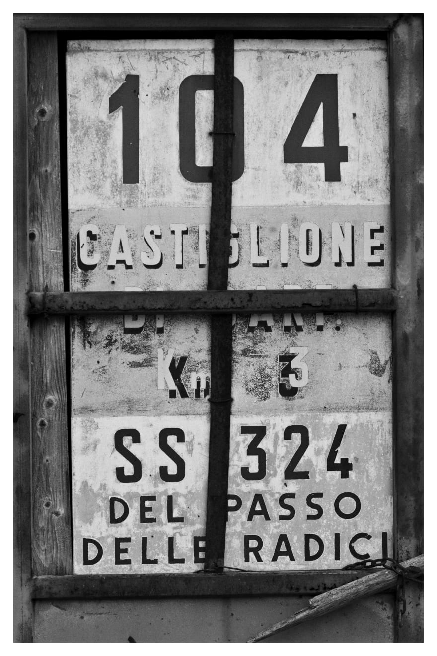 Black and white photograph of an old road sign in Tuscany, Italy.