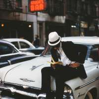 Man with white Hat reading on a car, NYC
