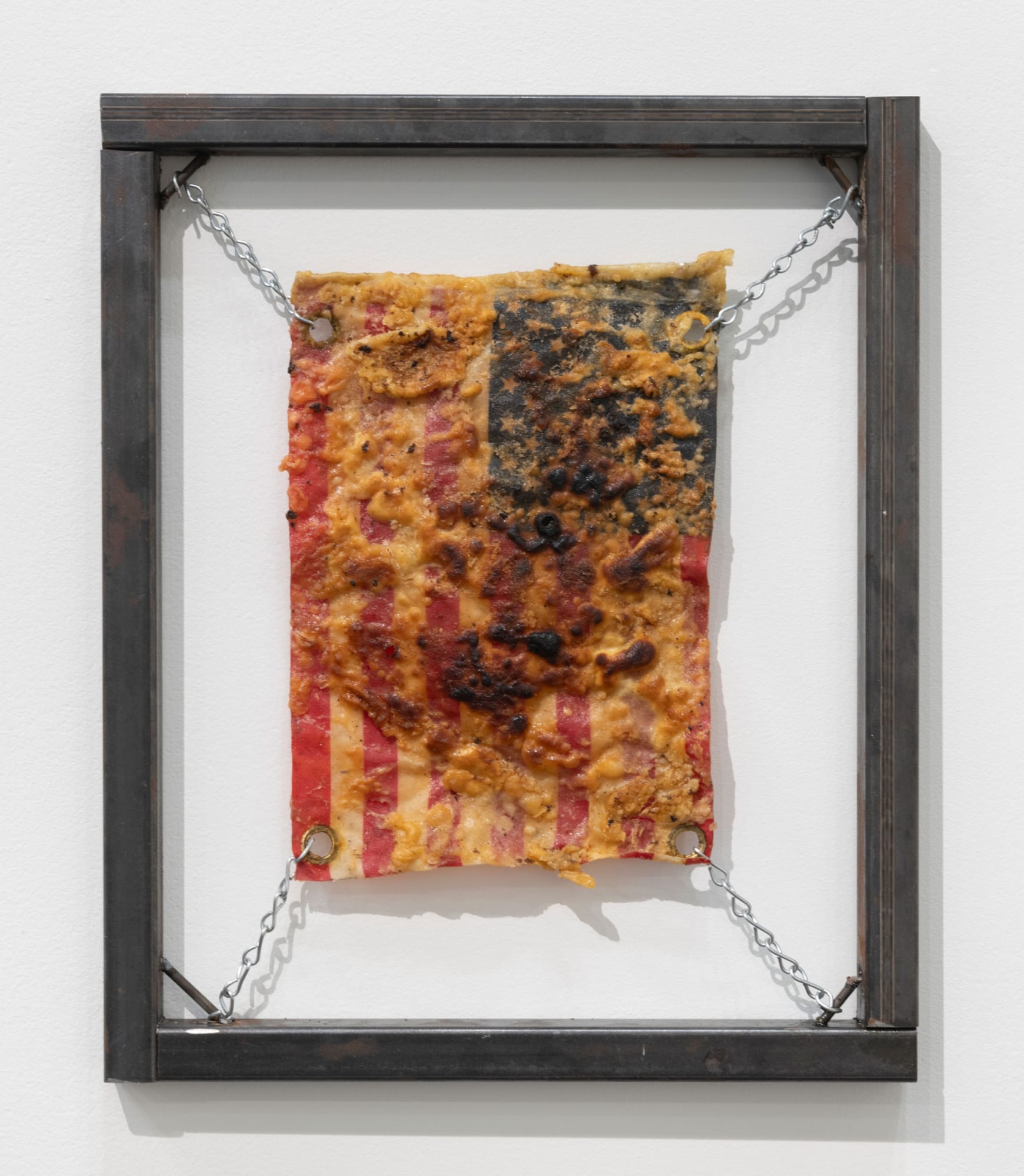 Kiyan Williams Sauteed and Suspended Flag, 2023 Nylon flag, adobo, anise, cardamom, crushed red pepper flakes, chili powder, eggs, flour, seasoning salt, sazón, smoked cocoa, soybean oil, resin, steel tube, steel chain 18 x 15 in 45.7 x 38.1 cm Photography by Adam Reich