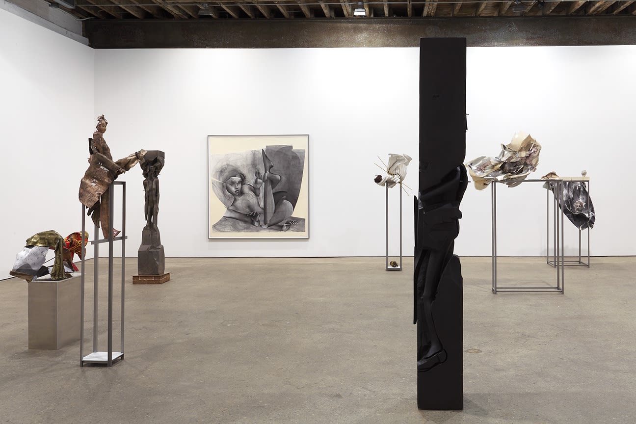 Installation view of Matthew Monahan's sixth solo show at Anton Kern Gallery, featuring sixteen sculptures, a set of drawings, two wall-mounted masks, and a single large figure in the back room. Detail of column with works in the back.