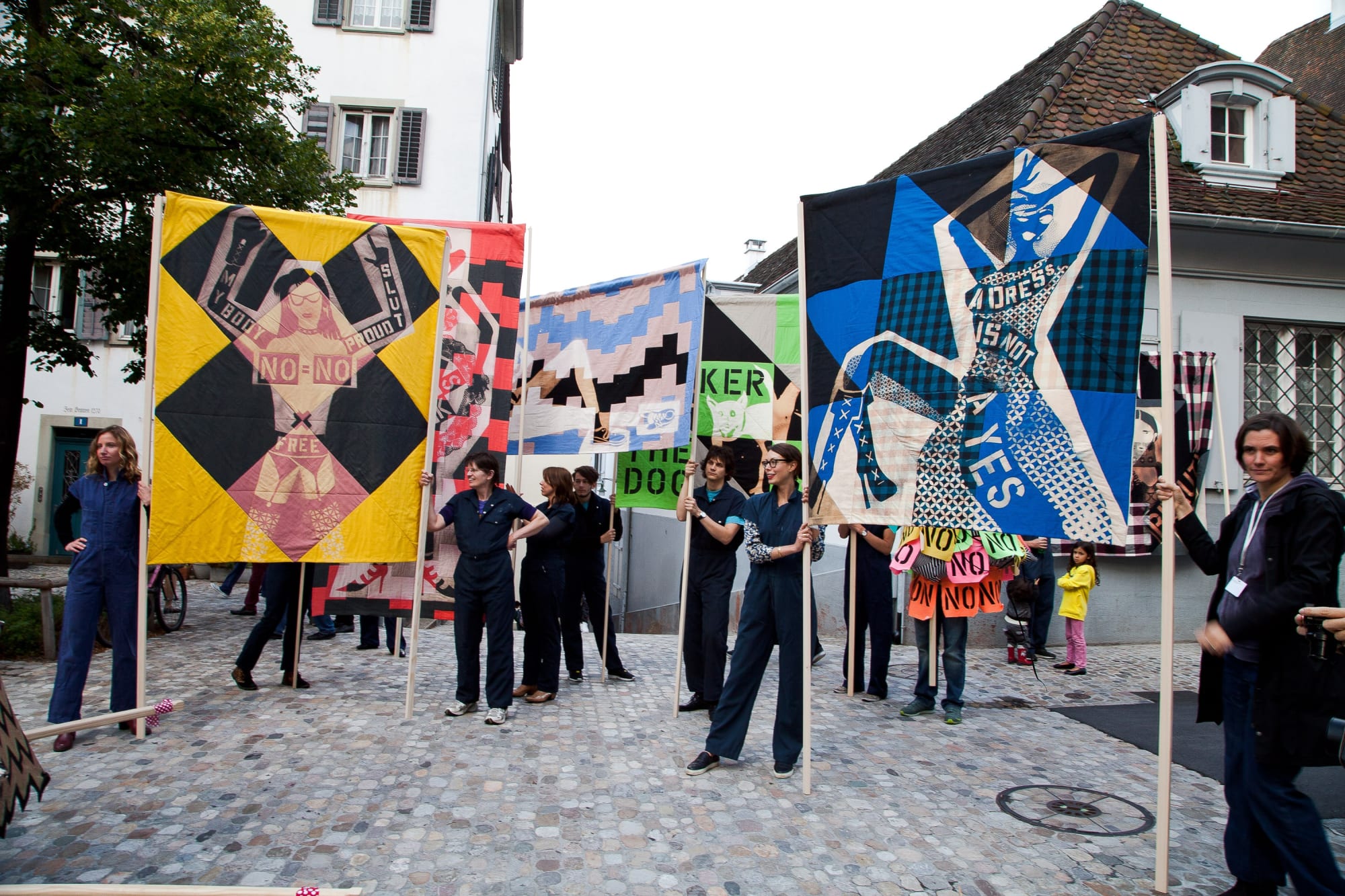 Installation view of Lara Schnitger's show at Basel Parcours, featuring a large body of works as well as a procession through Mezzeplatz. Multiple flat, cotton, linen works held in the air via wooden poles.