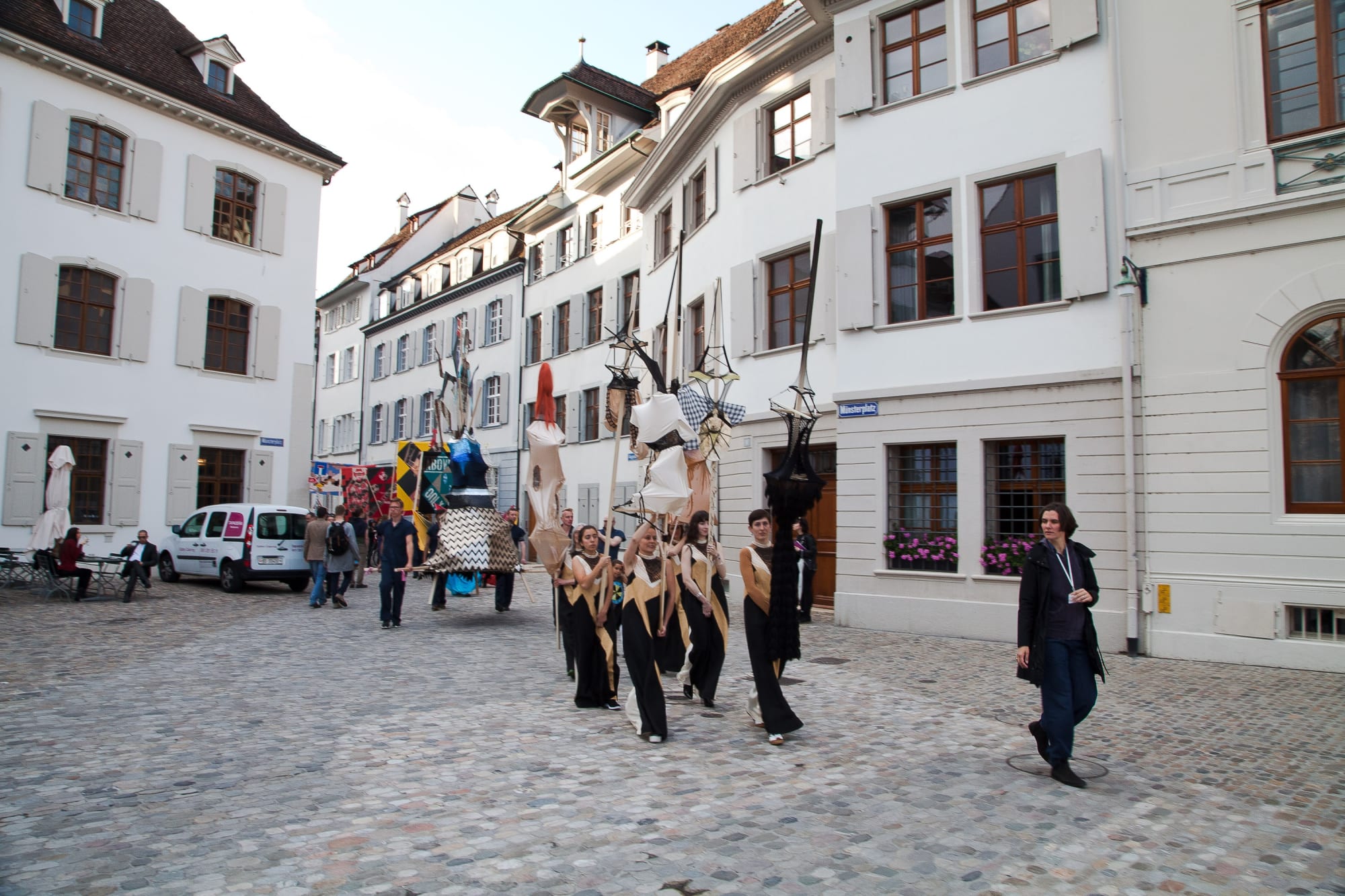 Installation view of Lara Schnitger's show at Basel Parcours, featuring a large body of works as well as a procession through Mezzeplatz. The procession circles back around to face a crowd of people.