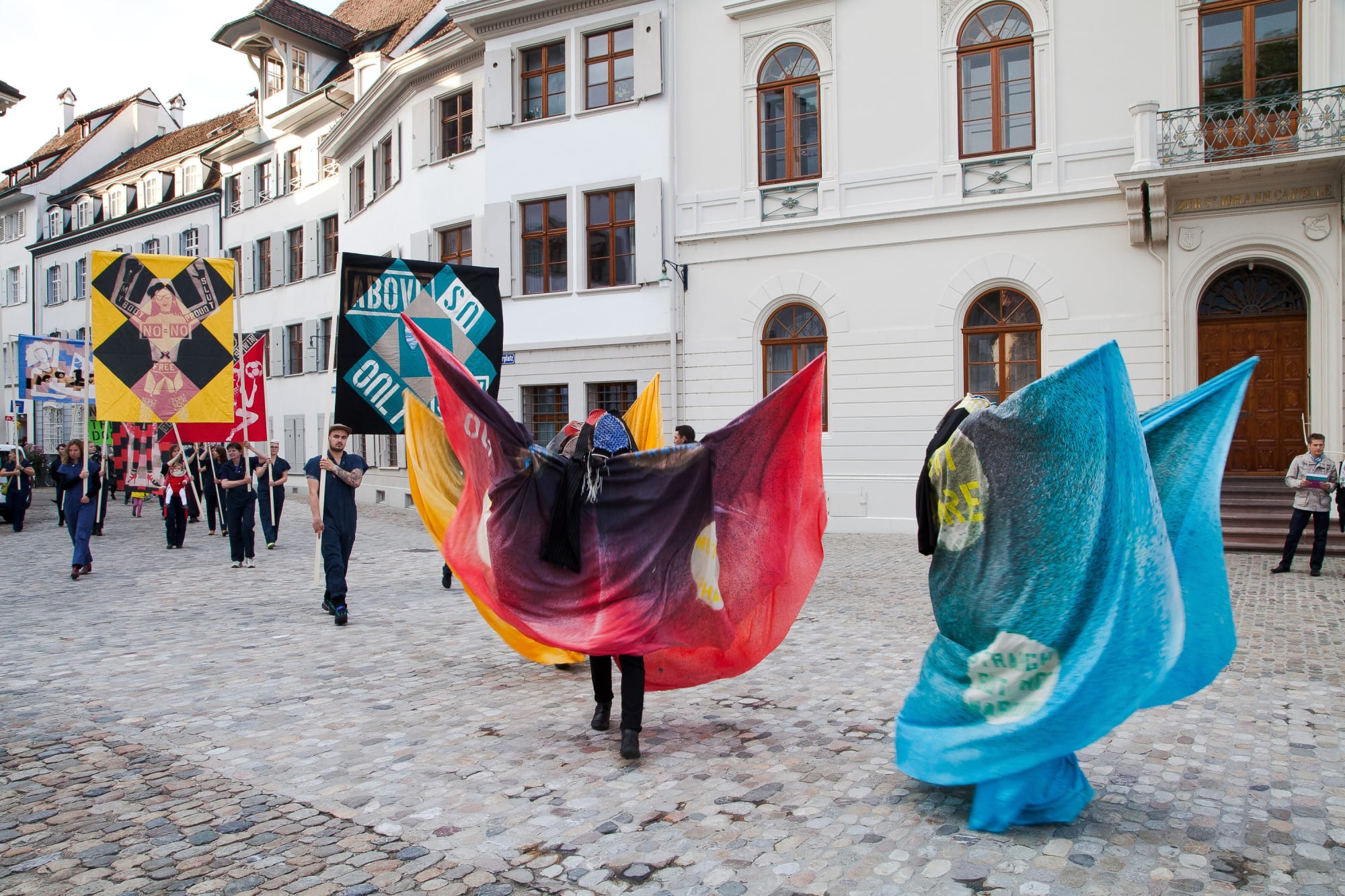 Installation view of Lara Schnitger's show at Basel Parcours, featuring a large body of works as well as a procession through Mezzeplatz. Marchers and works make their way toward the center of Basel.
