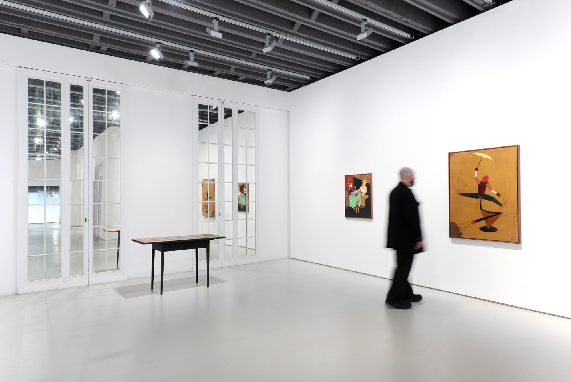 Corner view 2 including mirrored doors, visitor in dark clothing for scale, dark table, and two paintings.