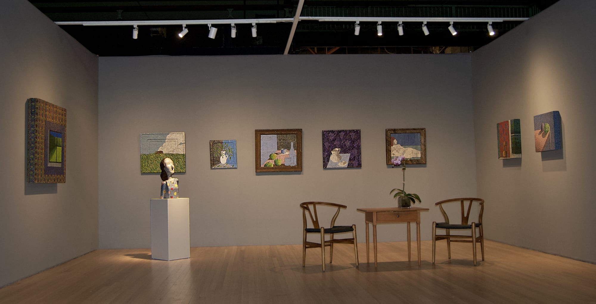 A room with eight paintings on the wall, one sculpture of a woman's bust on a pedestal, and a table and two chairs with an orchid sitting on the table
