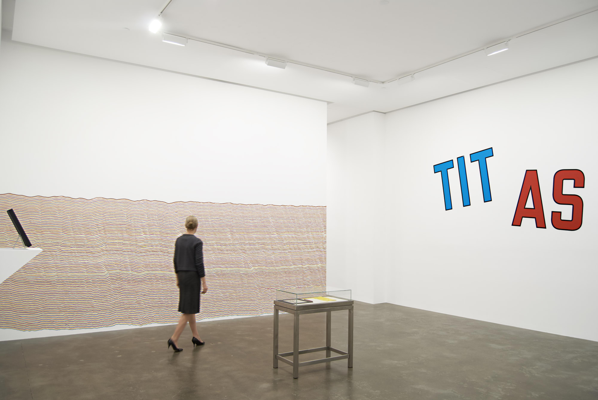 Gallery owner and Director, Susan Inglett, walks through D.I.Y. exhibition. In the background, Sol LeWitt's Wall Drawing #869 and Lawrence Weiner's TIT AS TAT.