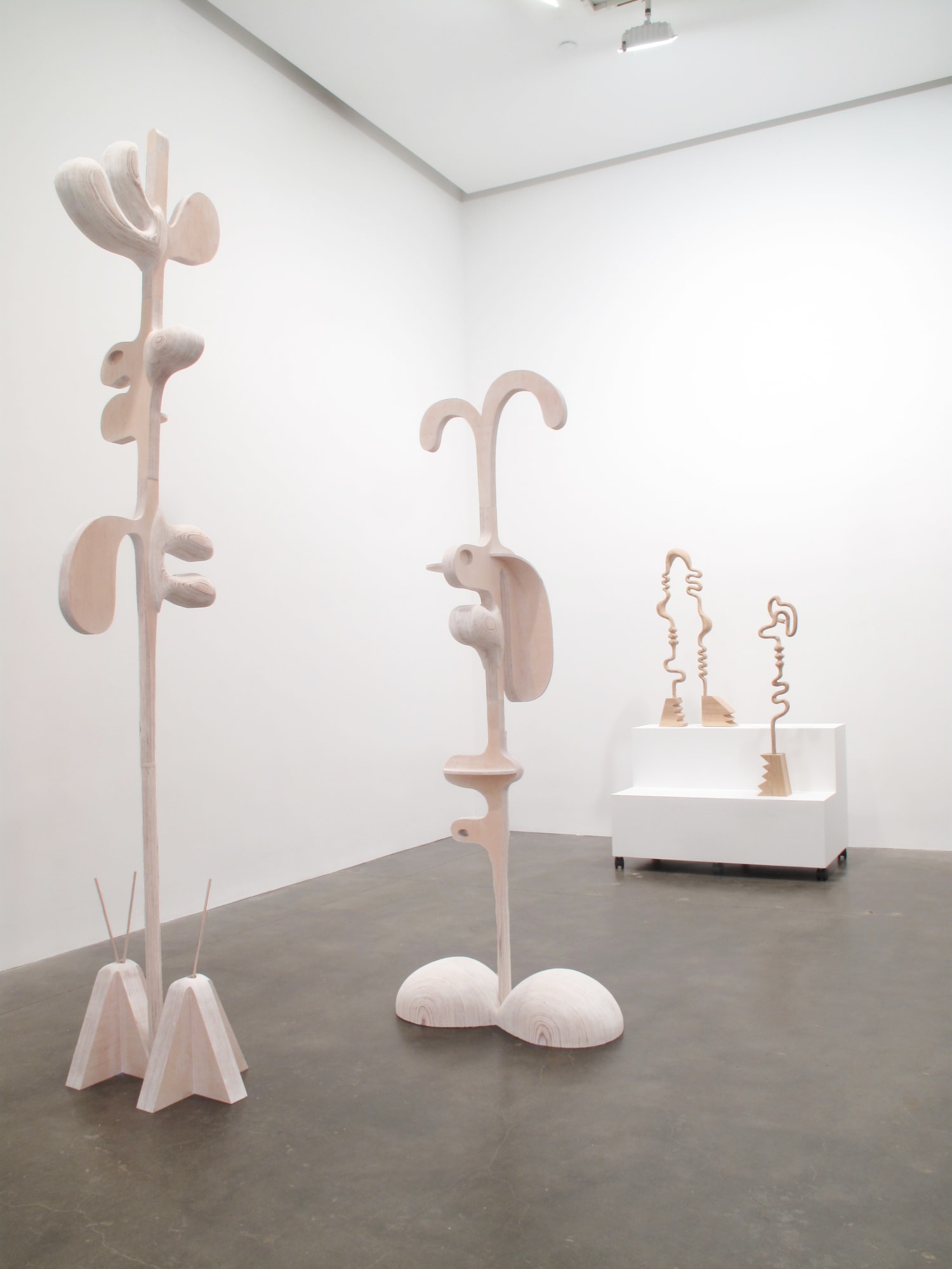 Installation view of Susan Inglett Gallery with three tall carved wooden sculptures with cartoon anatomical details in the foreground
