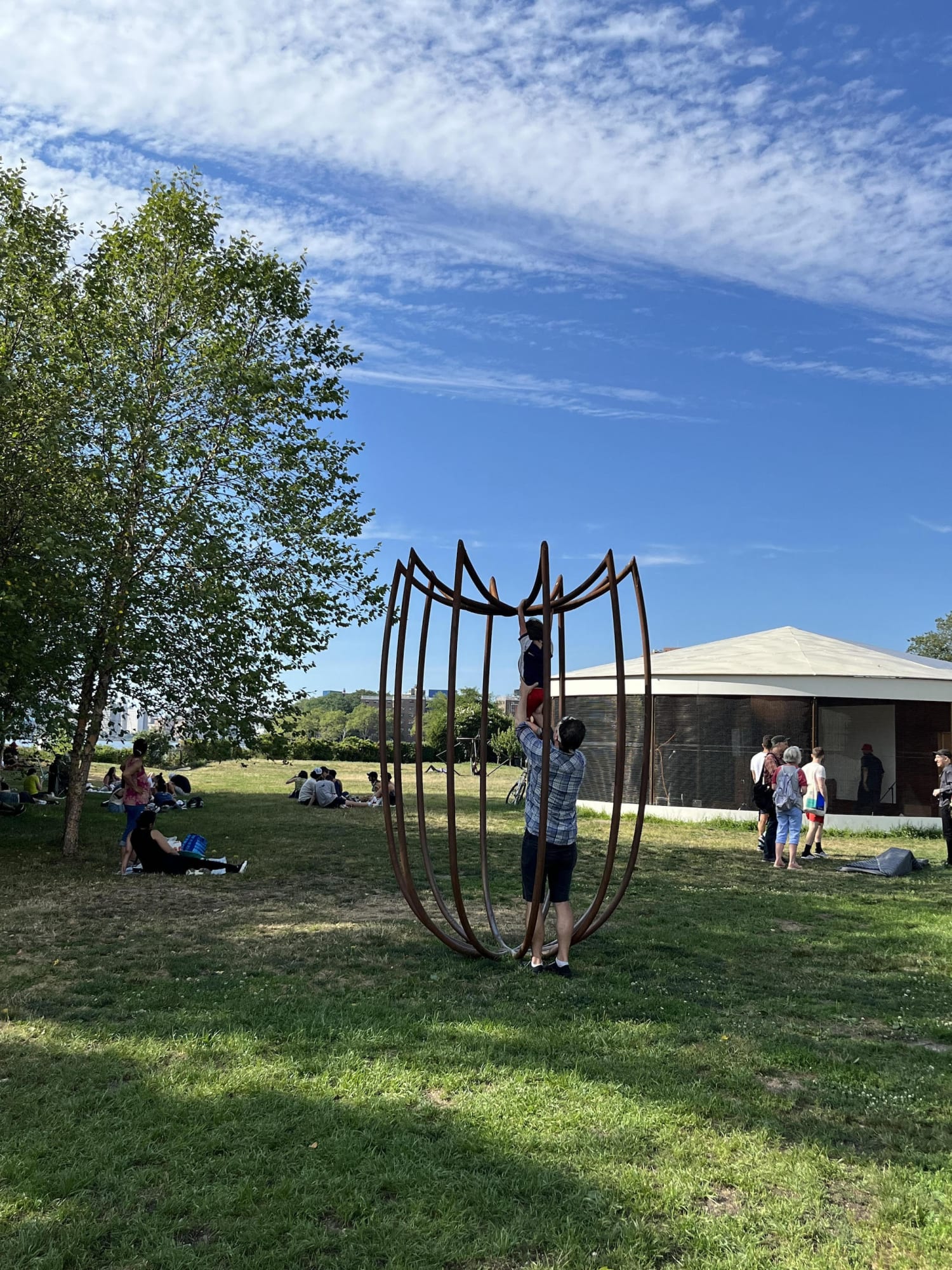 Outdoor installation view of a metal sculpture that resembles a an upside down umbrella at Socrates Sculpture Park