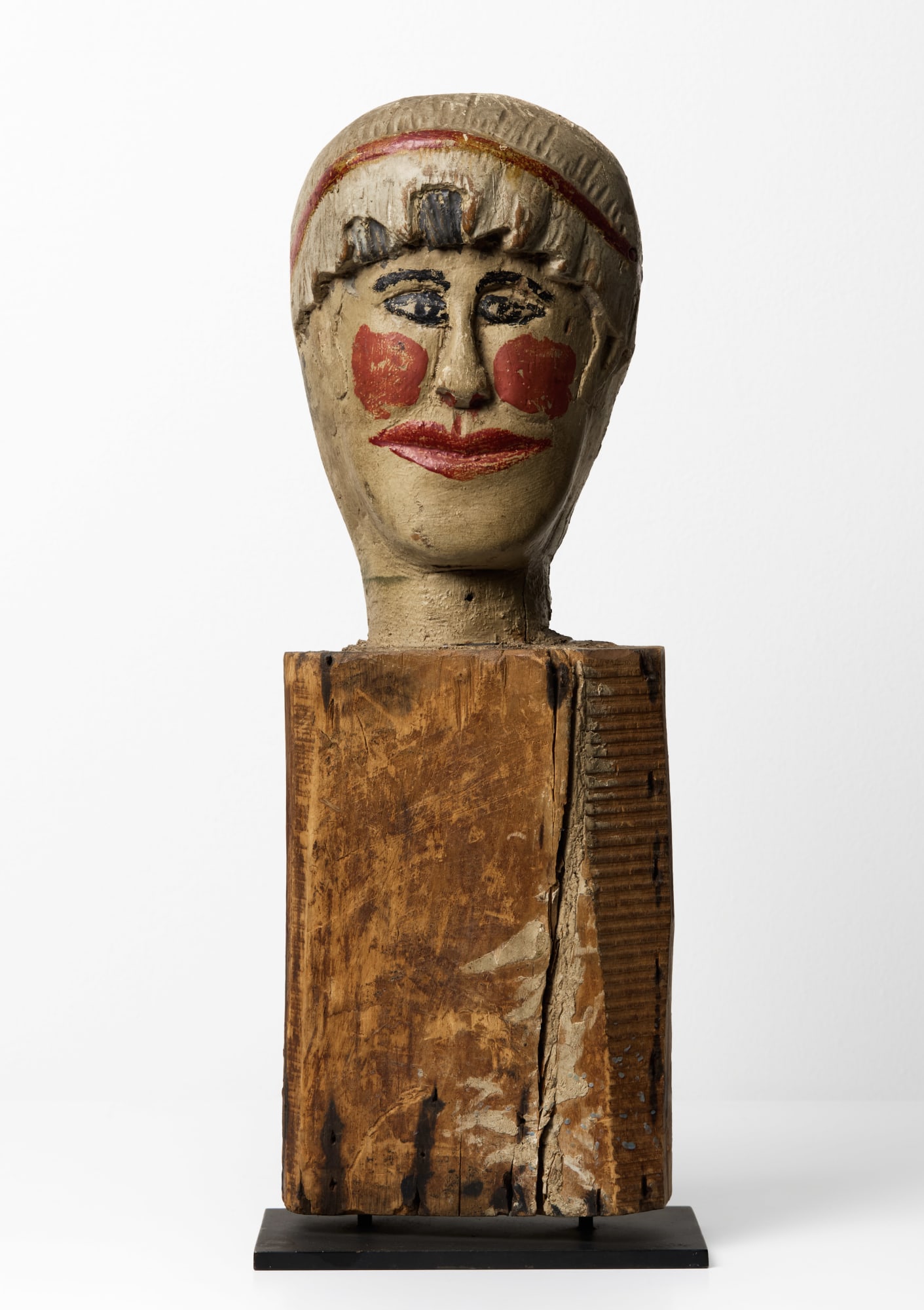 Carnival Knock Down Figure, late 19th - early 20th century Carved and painted wood 16 x 5 x 4 in. (40.6 x 12.7 x 10.2 cm) (ArU 494) $ 4,500 ••• Carved from solid wood and painted with rouged cheeks, red lips, and kohl-dark eyes, this anonymous carnival knockdown figure turns a game-piece into a personality. Its bright, theatrical face sits atop a roughly hewn block scarred by age, nails, and impact—evidence of a working life on an amusement midway, where it would have been repeatedly toppled and reset for players’ throws. The contrast between the jaunty, clownlike visage and the battered support gives the piece its charge: a target meant to be hit, yet rendered with surprising care and empathy. Removed from its original context and placed on a stand, it reads less as expendable equipment and more as a small, stubborn survivor of popular entertainment—part sculpture, part collaborator in countless vanished nights of noise, laughter, and competition.