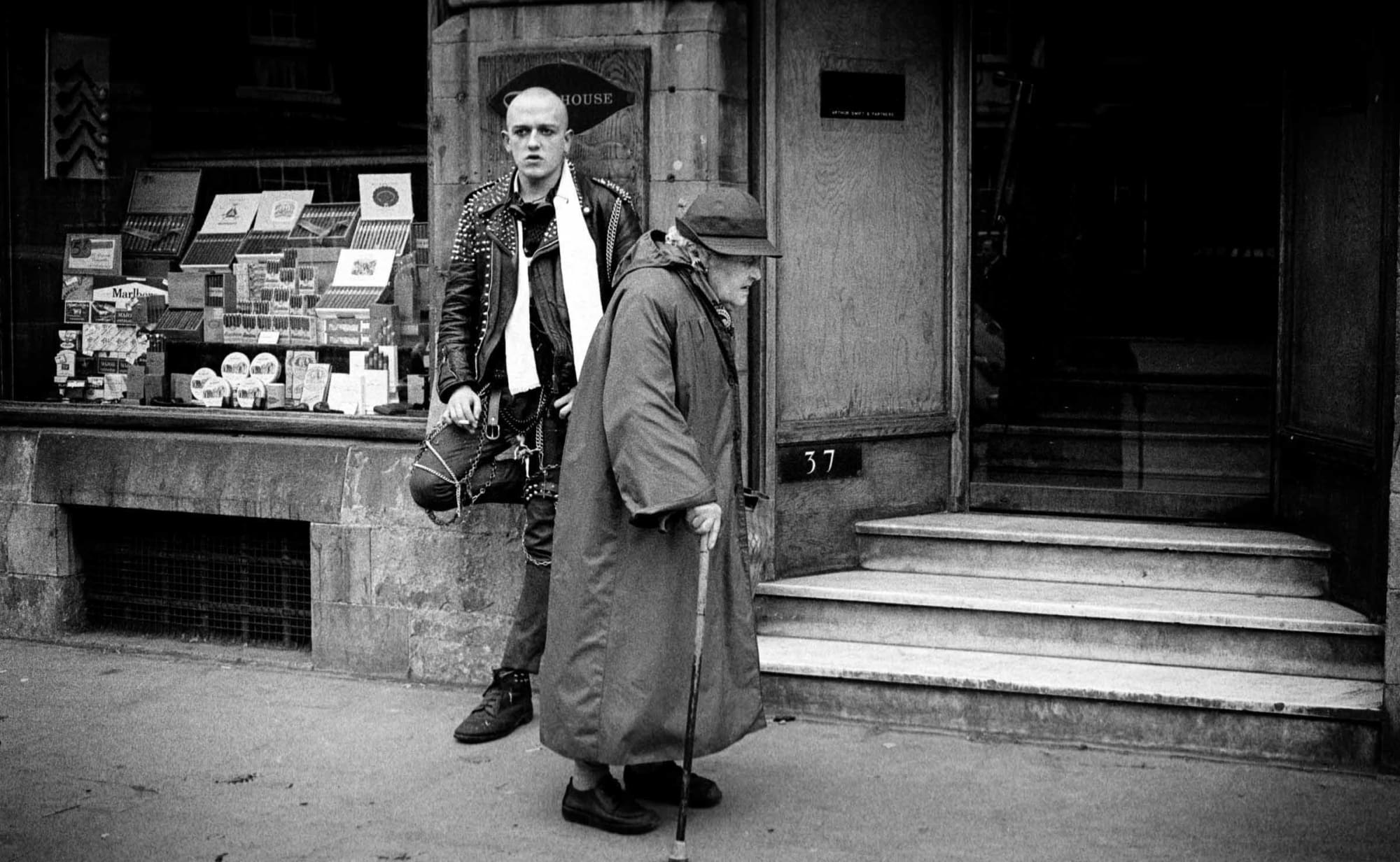 Street Fashions. An elderly woman passes by a young punk on College Green in Dublin, Ireland. 1981. Photo: © Eamonn Farrell