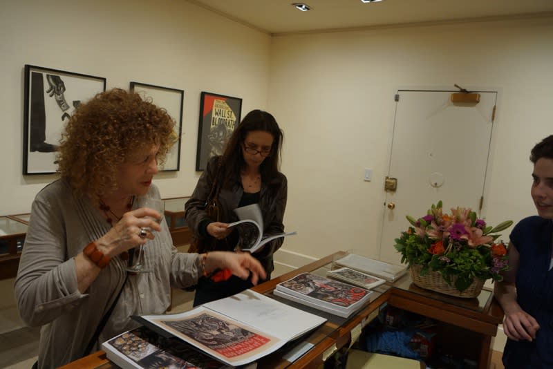 Photograph of visitors flipping through Coe's new book "Cruel" by the front desk at the opening of the exhibition "Mad as Hell," 2012