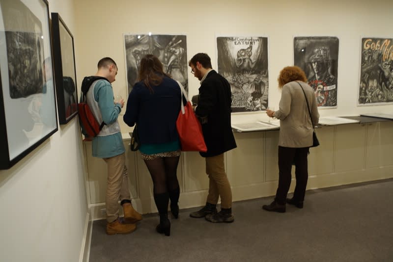 Photograph of gallery visitors looking through binders of Sue Coe's prints at the opening of the exhibition "Mad as Hell," 2012