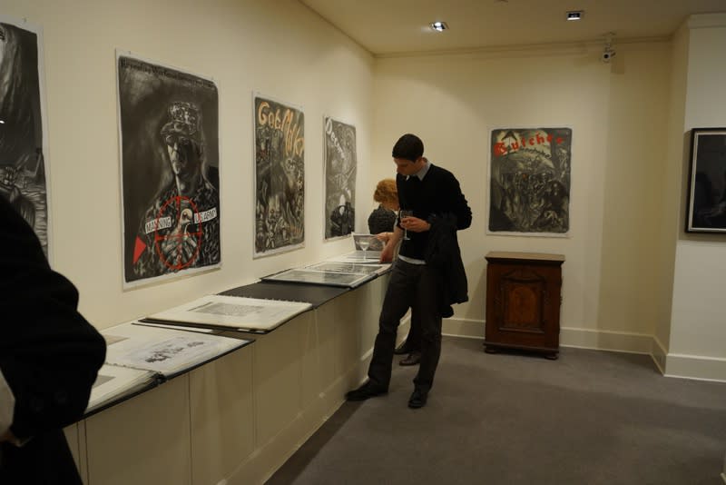 Photograph of visitors looking at prints at the opening of the exhibition "Mad as Hell," 2012