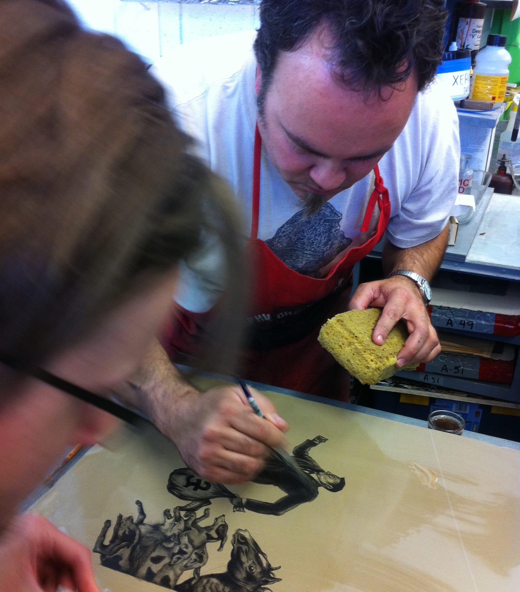 Two printers stand on either side of the lithographic plate with brushes and sponges in hand