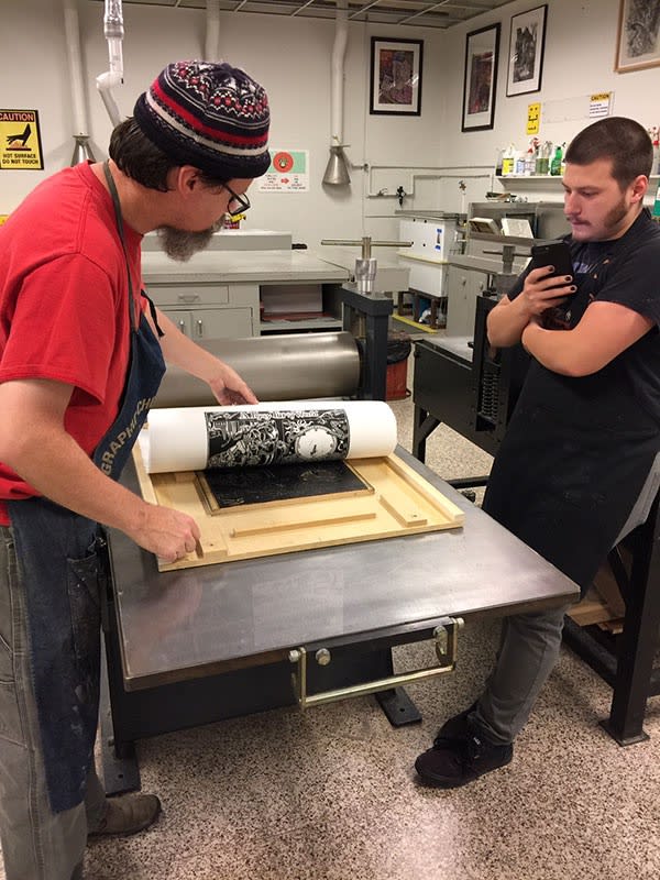 Photograph of master printer Brian Kelly and student pulling an impression of "A Topsy Turvy World," 2018, from the printing press