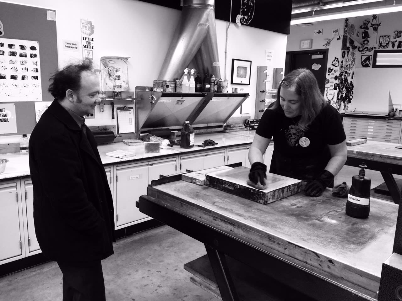 One printer spreads ink on the plate while another printer stands nearby