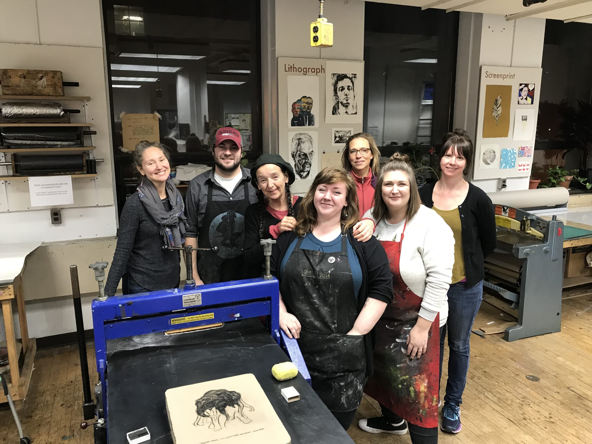 Photograph of Sue Coe and the amazing print team at Kendall College of Art and Design of Ferris State University stand behind the new lithograph produced during a 2017 visiting artist program