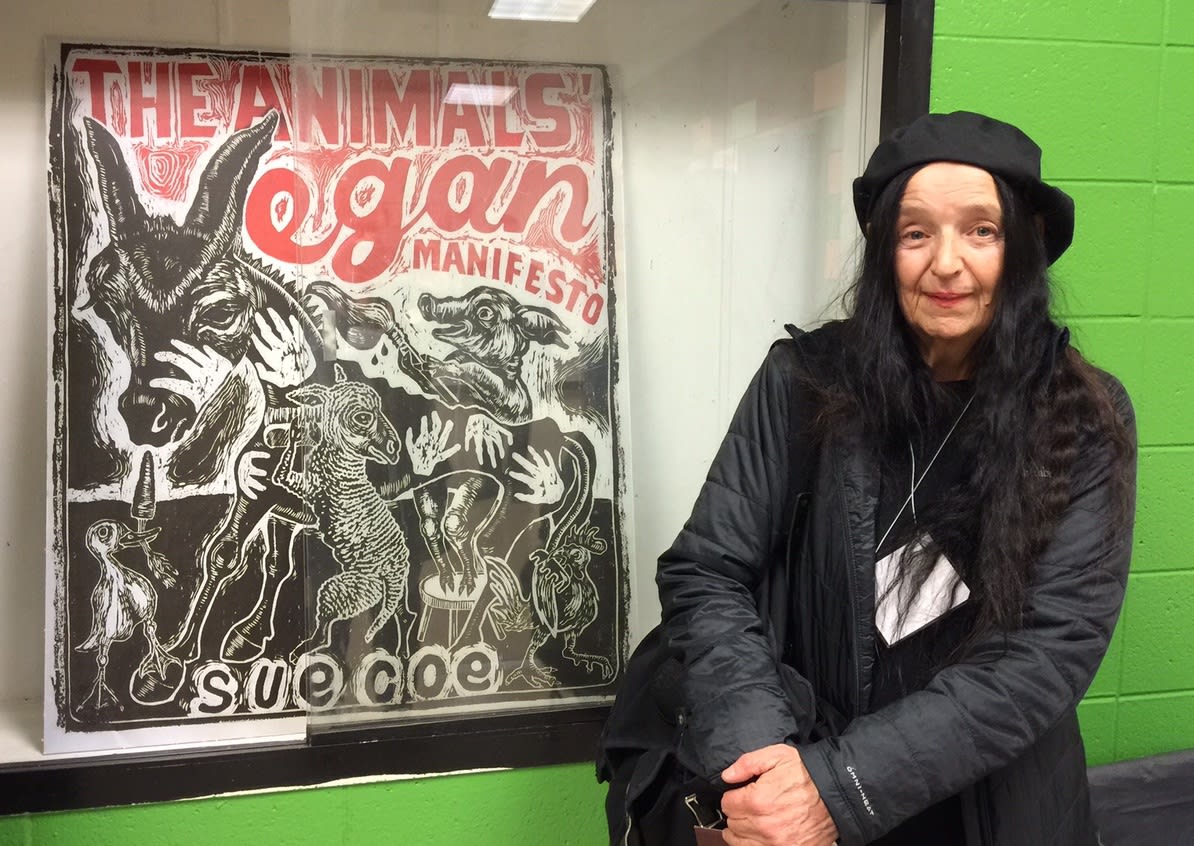 Photograph of the artist sitting in front of a poster for the exhibition "The Animals' Vegan Manifesto," Welch School of Art and Design, GSU, 2017