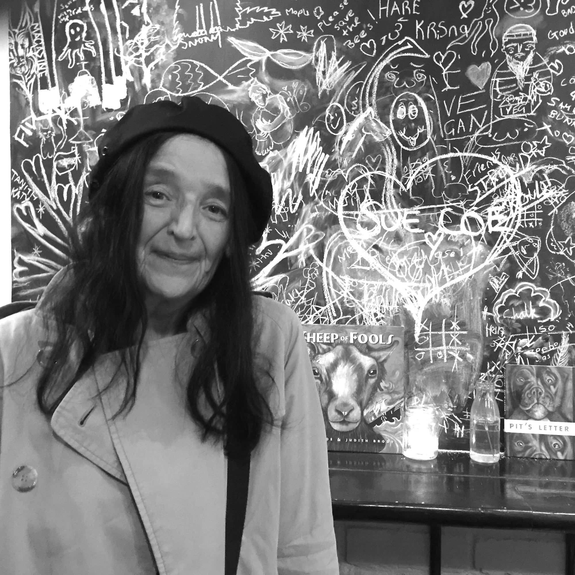 Photograph of the artist standing in front of a chalkboard, smirking.