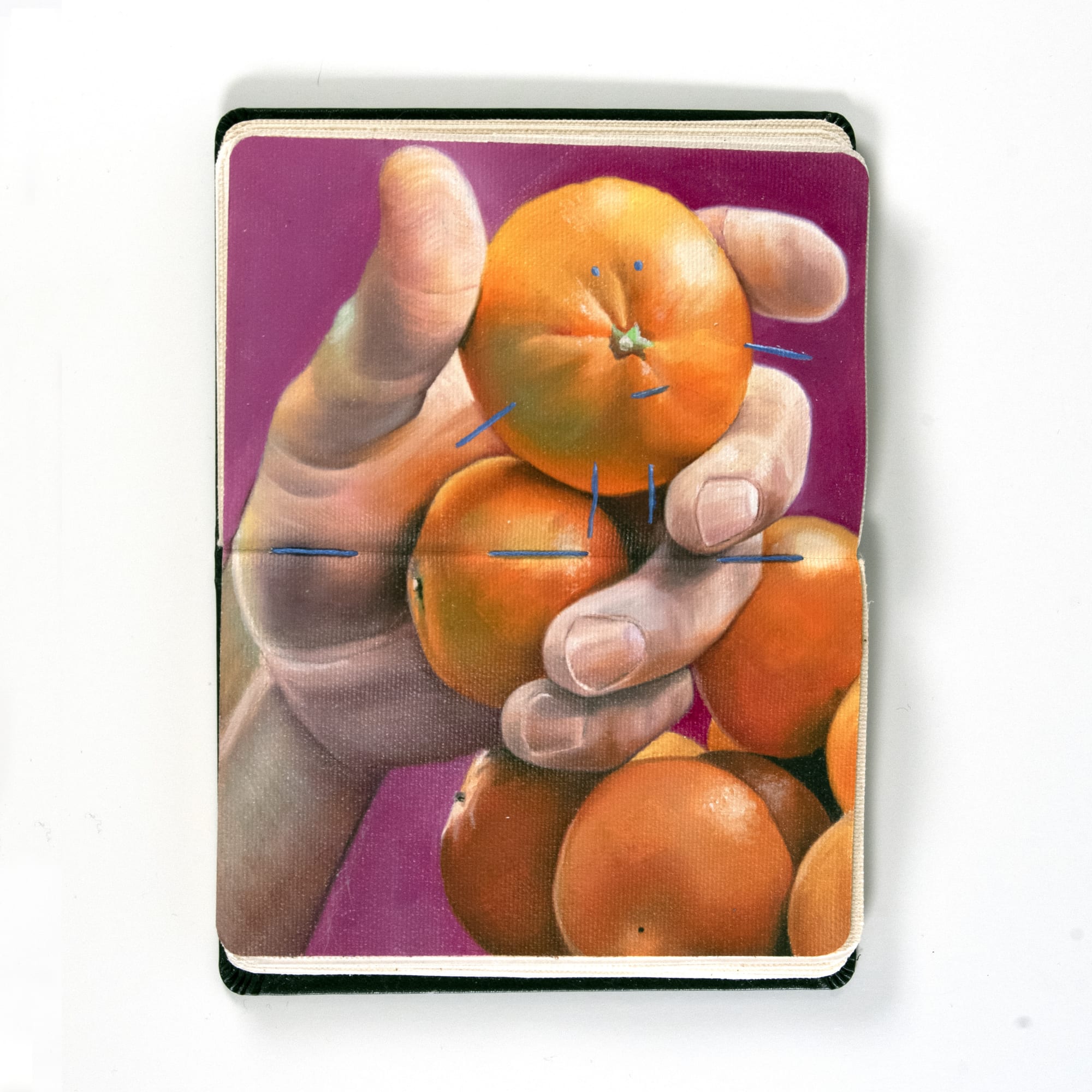 hand holding clementines over a pink background inside a moleskin notebook
