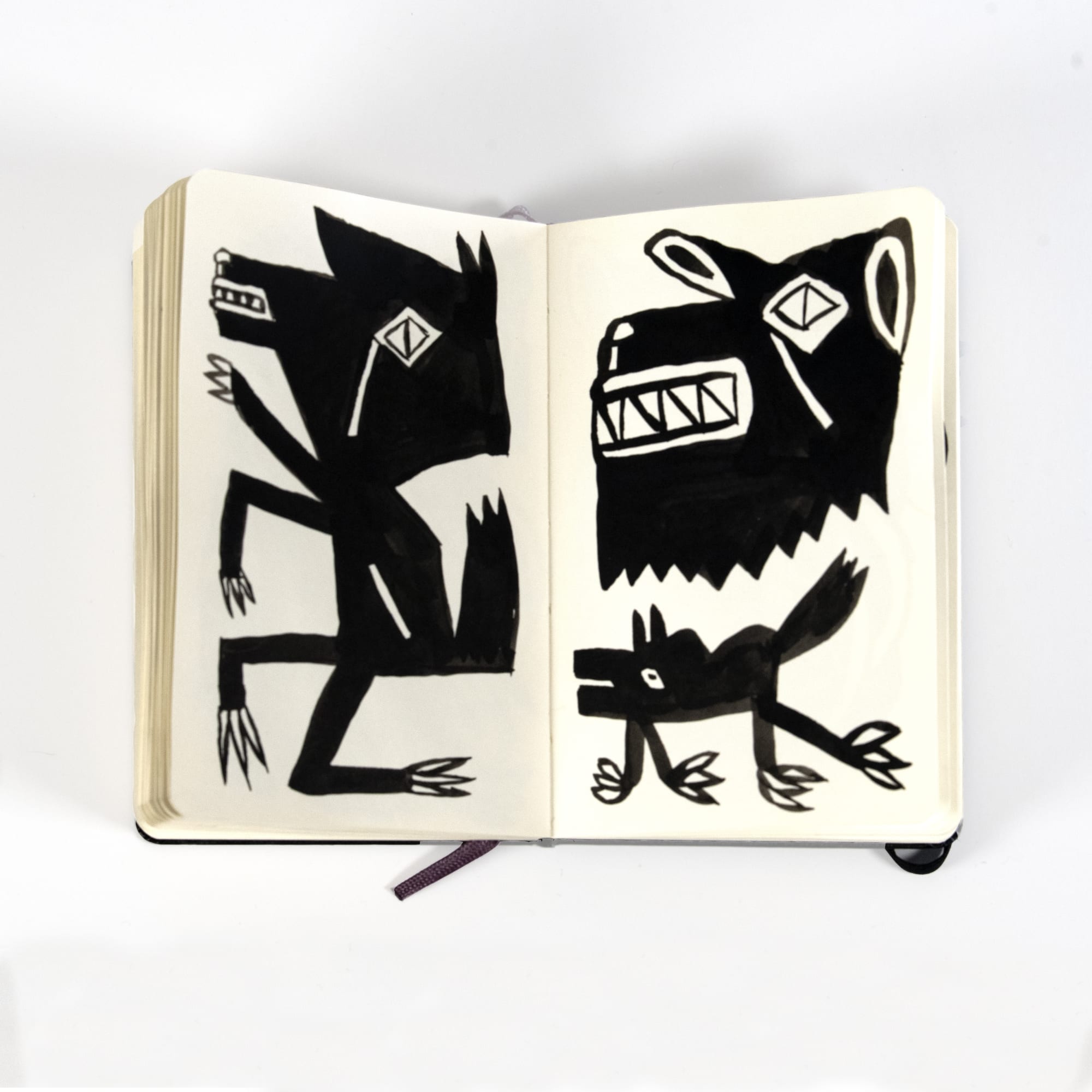 three angular black and white creatures drawn in a moleskin notebook