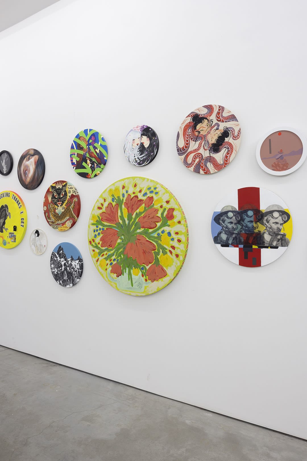 installation image of many round format artworks displayed on a white wall