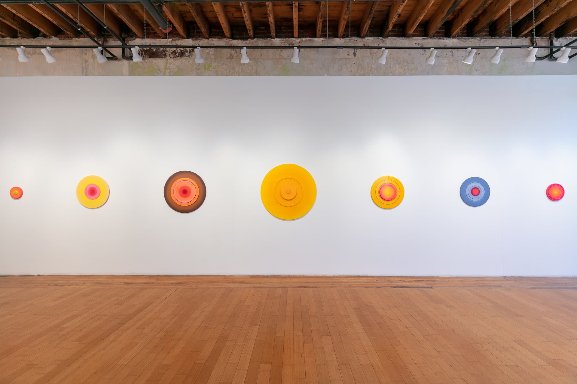 Installation shot of Future Maybe exhibition showing the right wall of the Main Gallery, on which hangs a series of circular resin wall sculptures. From left to right: Pacifier 6, 11, 13, 14, 12, 9, 8, 4, and 10.