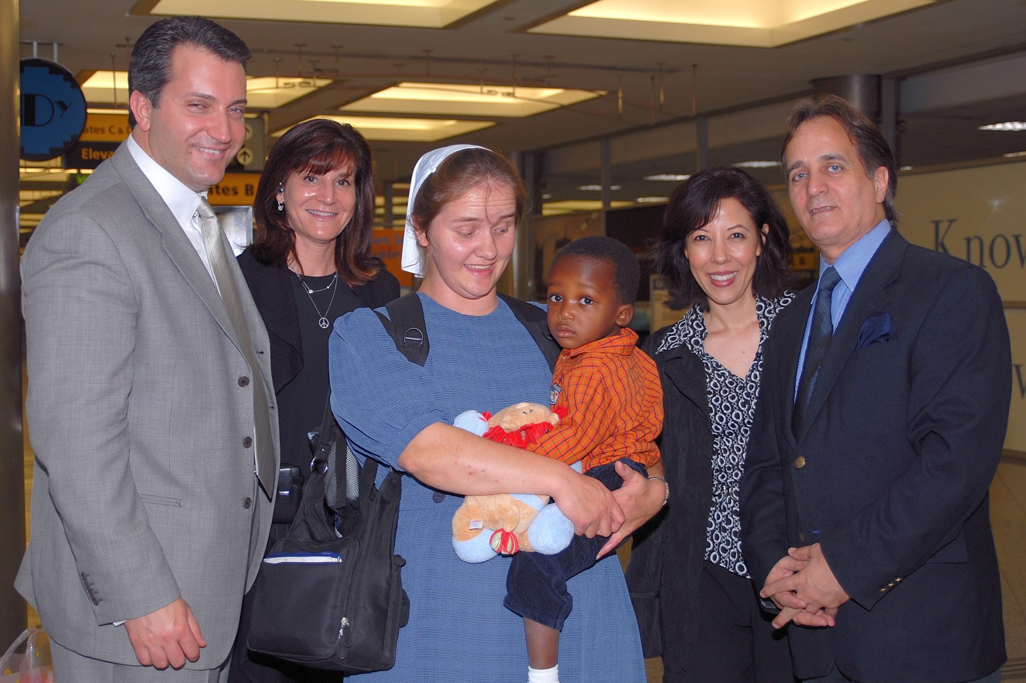 Group of two men and two women pose with a nun carrying a young child at JFK airport