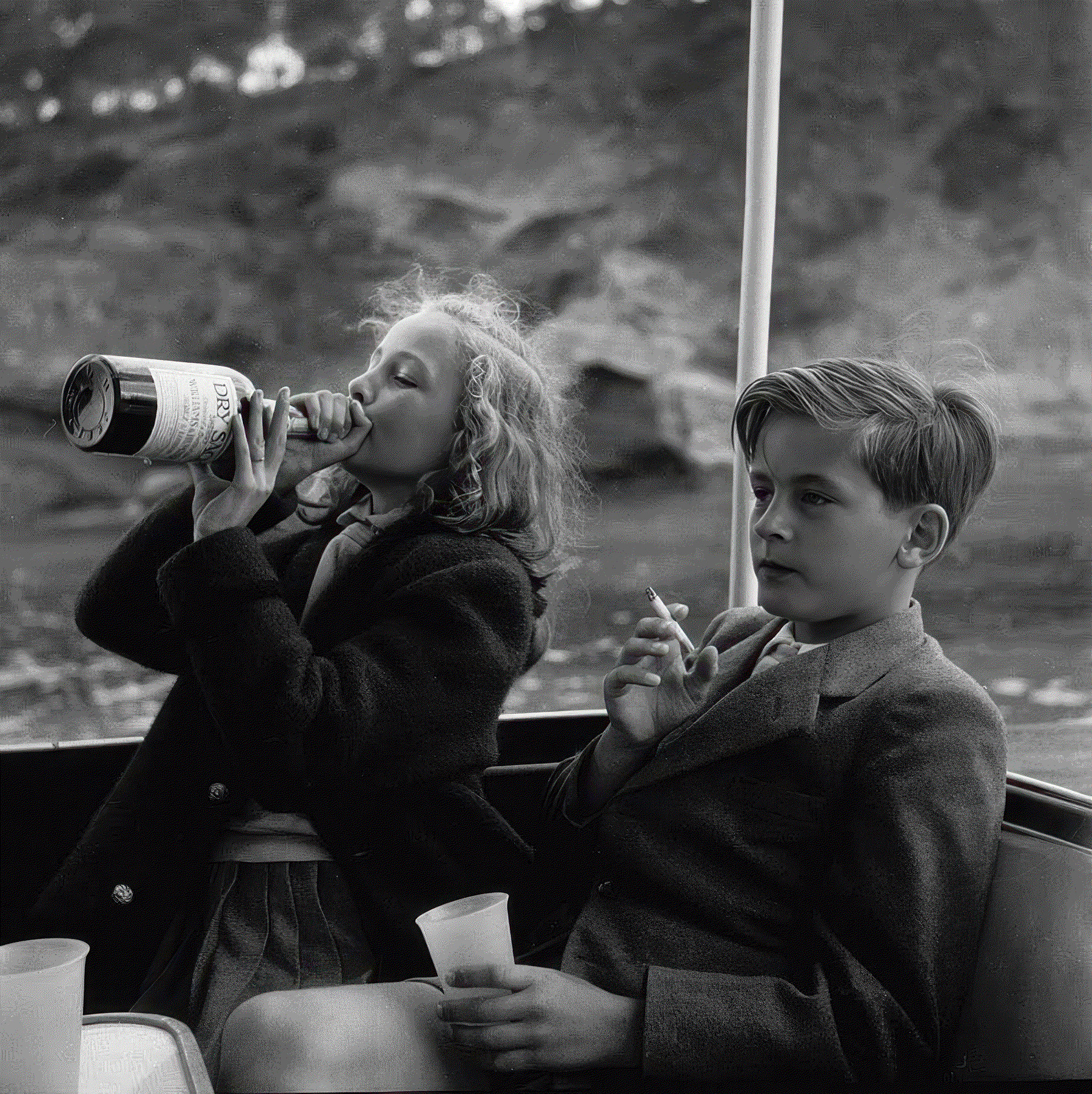 Black and white photograph of a young boy and girl drinking and smoking on a boat