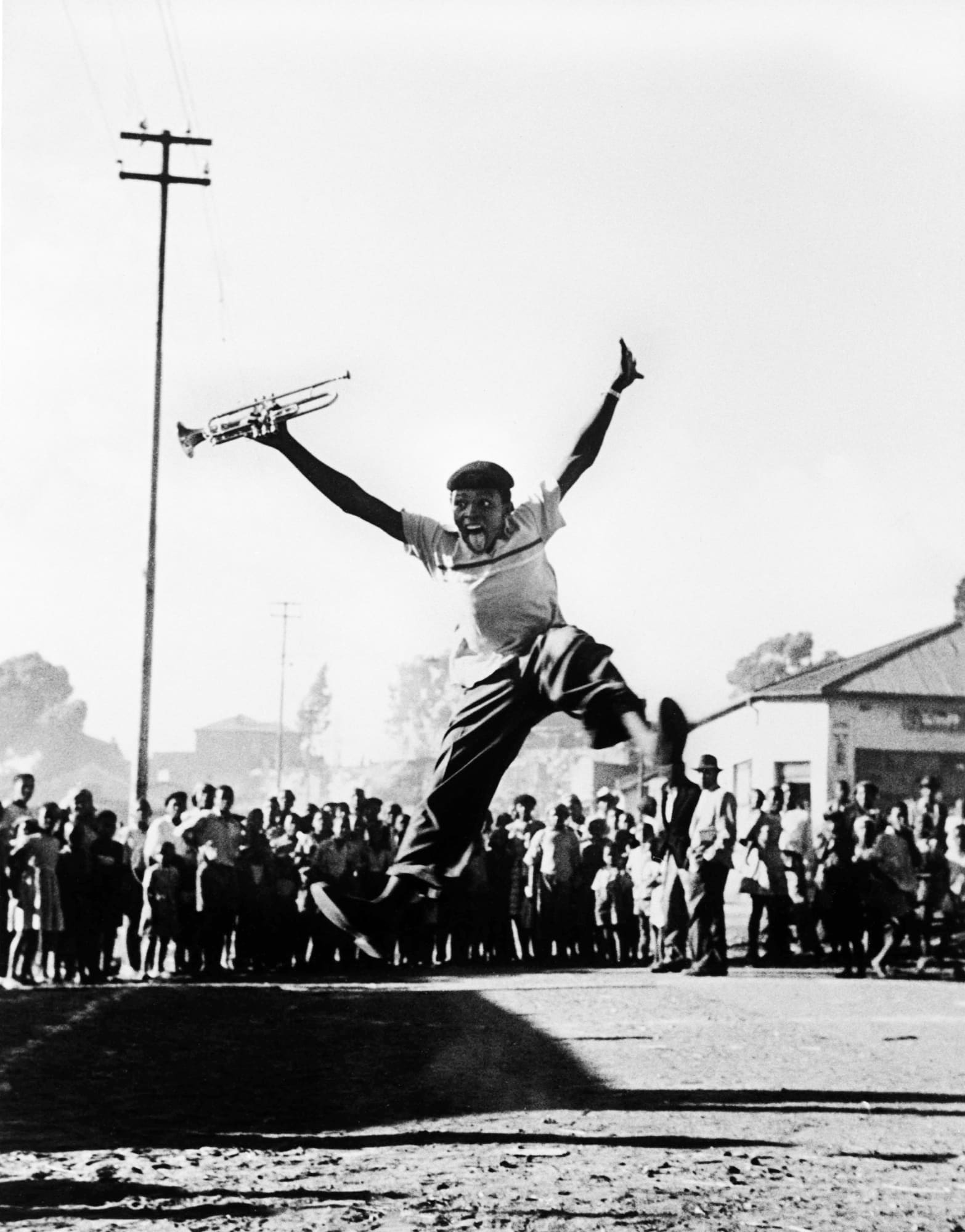 Alf Kumalo, Hugh Masekela leaps into the air with delight after recieving a trumpet from American jazz legend, Louis Armstrong, 1956
