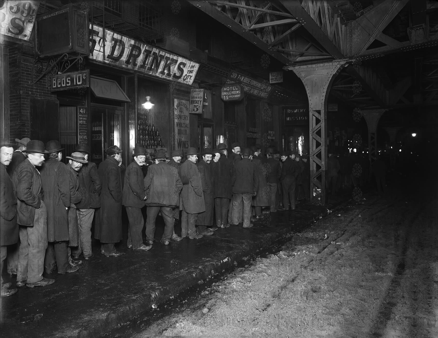 “The Breadline at Bowery Mission. A Rare Glimpse into the Struggles & Compassion of Old New York”: Step into the heart of Lower Manhattan, circa 1900, with this exceptional, large-format, limited-edition print, masterfully reproduced from an original vintage glass camera negative. This stunning image, possibly unpublished, captures a haunting yet deeply moving winter night scene outside the Bowery Mission at 39 Bowery Street—one of New York’s most enduring beacons of charity.