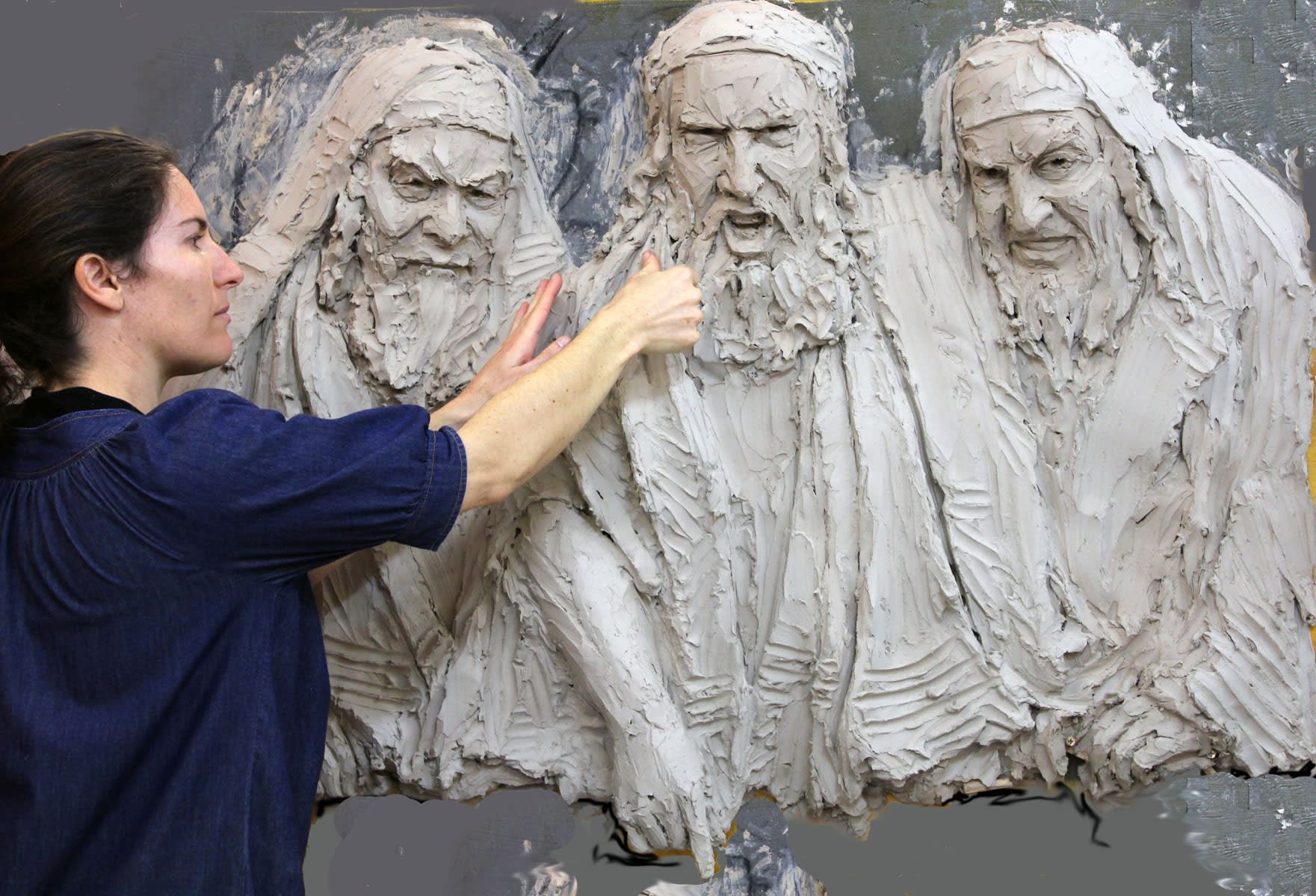 Linda Klarfeld sculpting the Sanhedrin in clay in her studio, showing the intricate detail of 3 angry faces in progress.