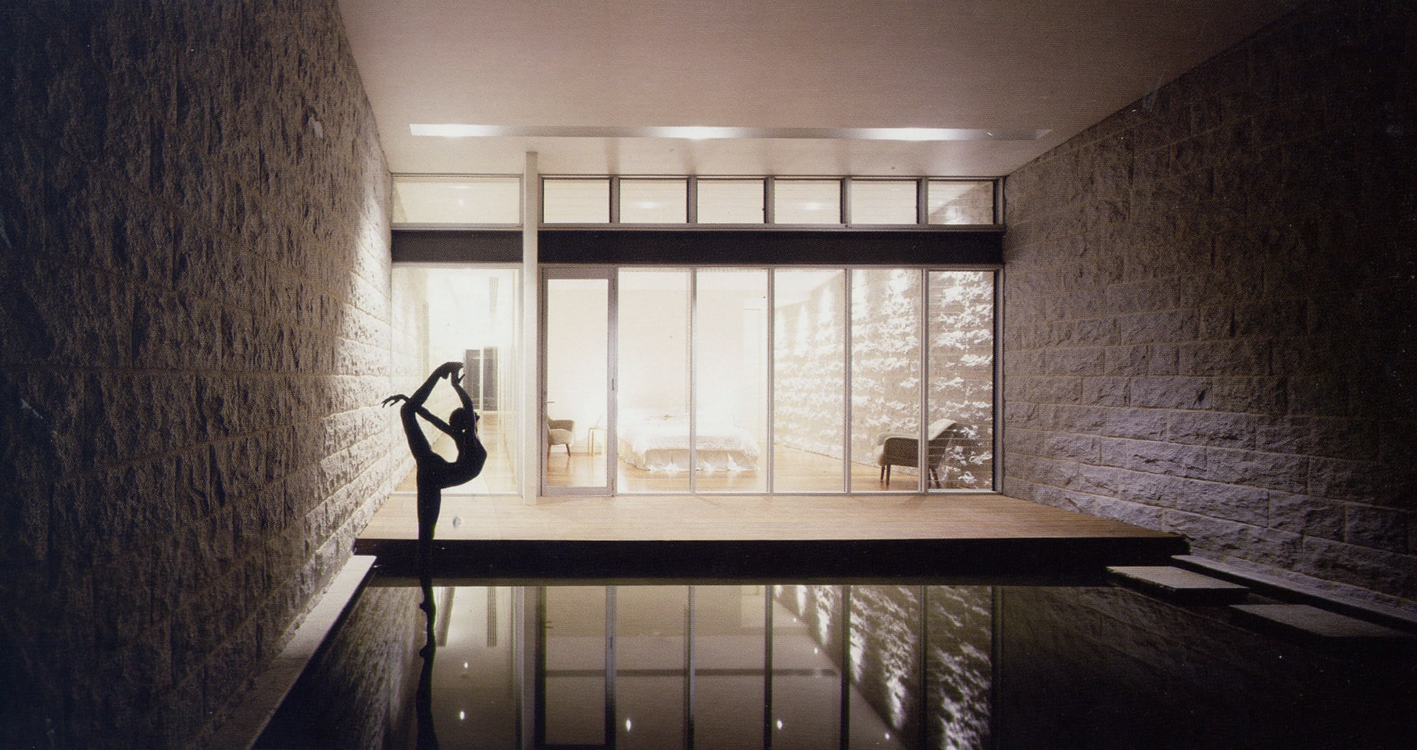A bronze sculpture of a ballet dancer standing en pointe on the water of a pond, set against the backdrop of a bedroom window.