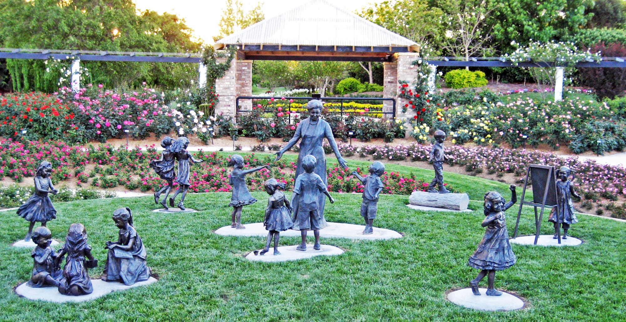 Expressions of Love Monument featuring a bronze sculpture of a grandmother surrounded by her grandchildren, set in the heart of a vibrant rose garden.