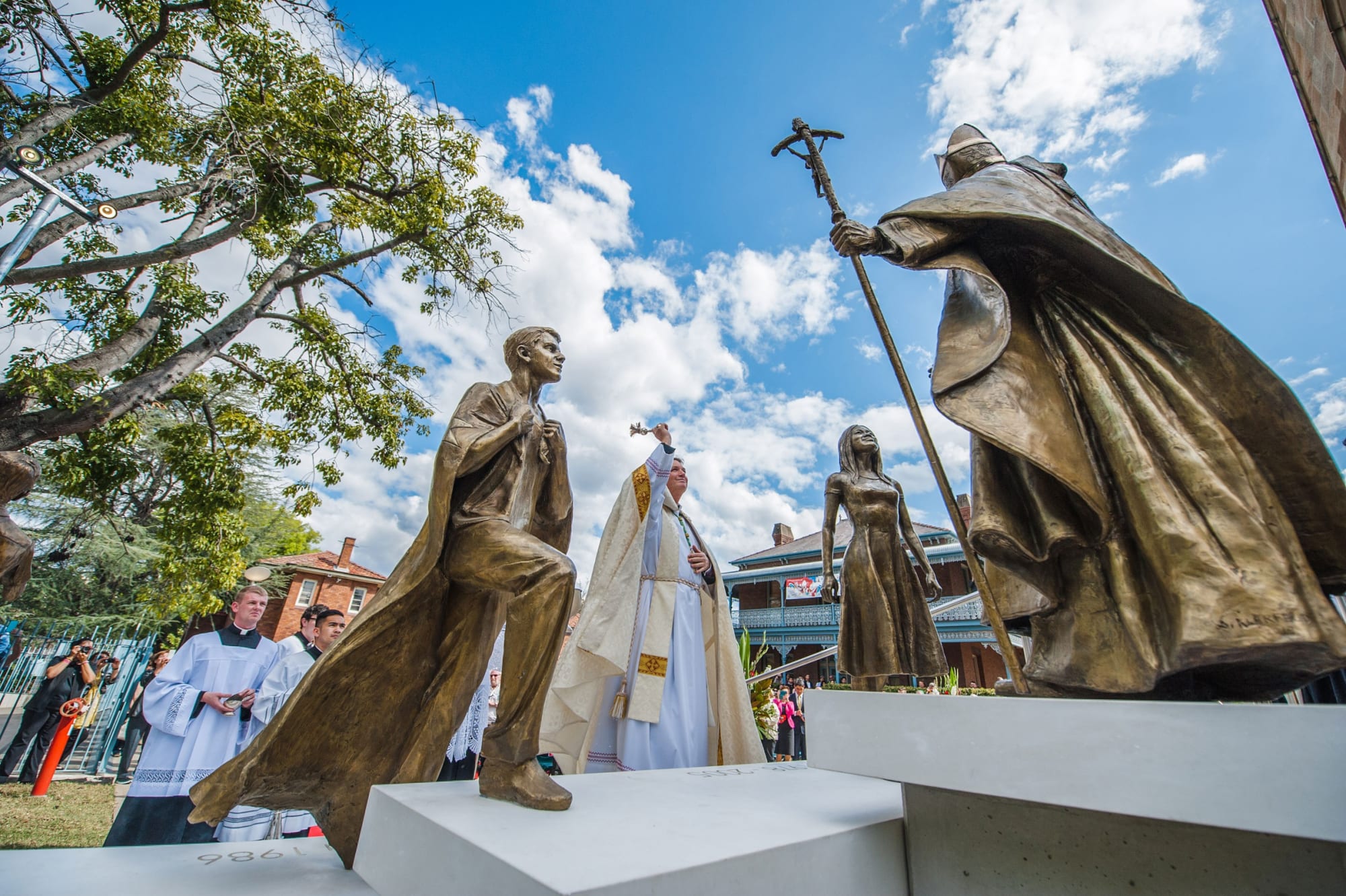 The Archbishop of Sydney blessing the monument of St. John Paul II outside St. Patrick's Cathedral, with a large audience in attendance.