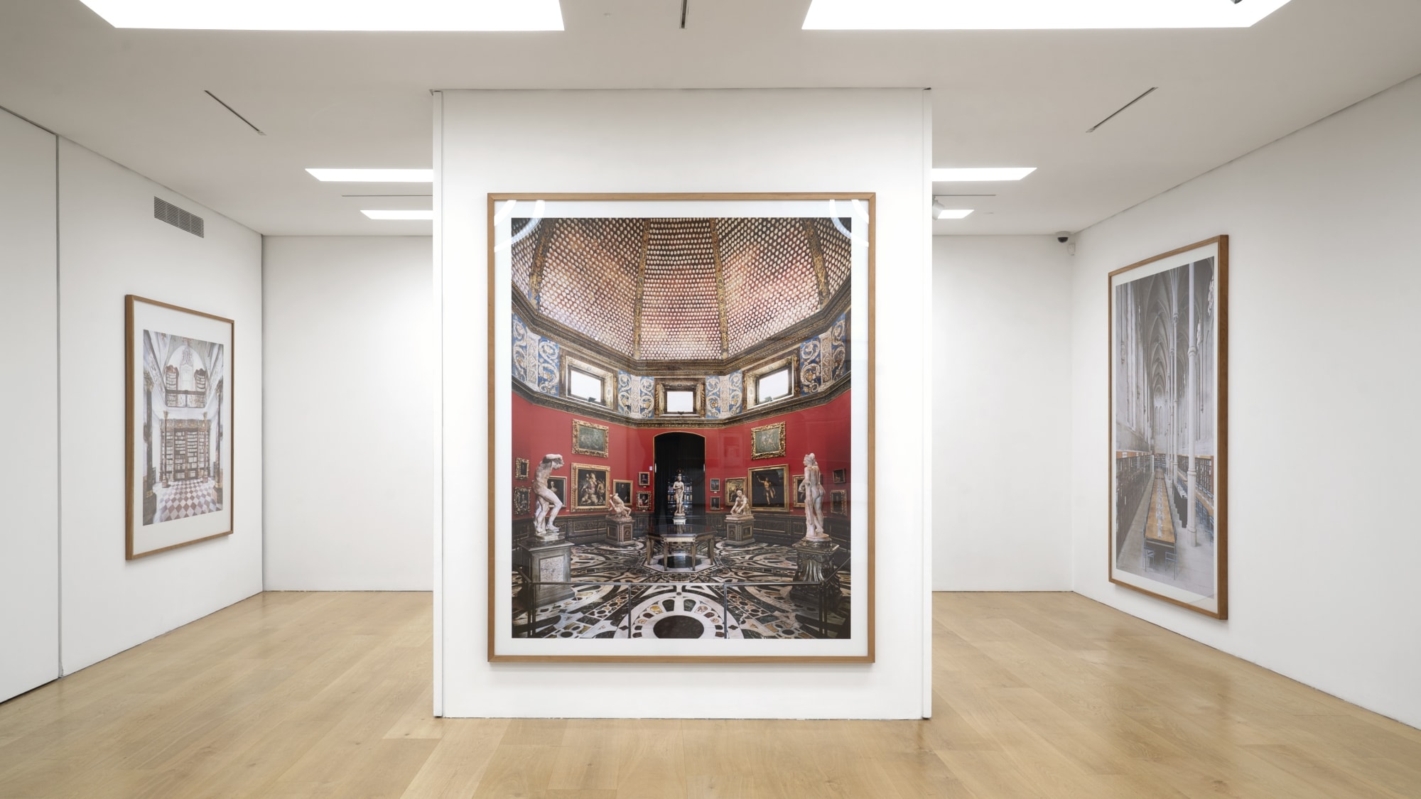 Installation view of a white cube gallery with wooden floors showing large scale framed photographs of interiors by Candida Hofer