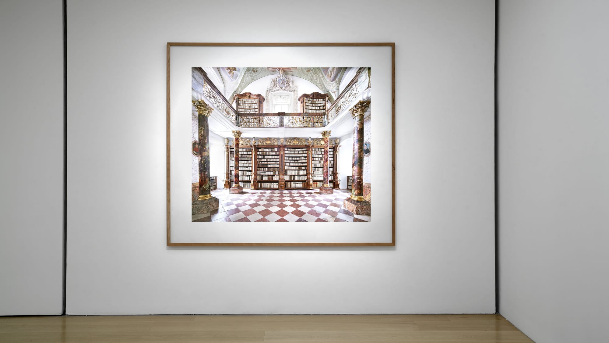 Installation view of a white cube gallery with wooden floors showing large scale framed photographs of interiors by Candida Hofer