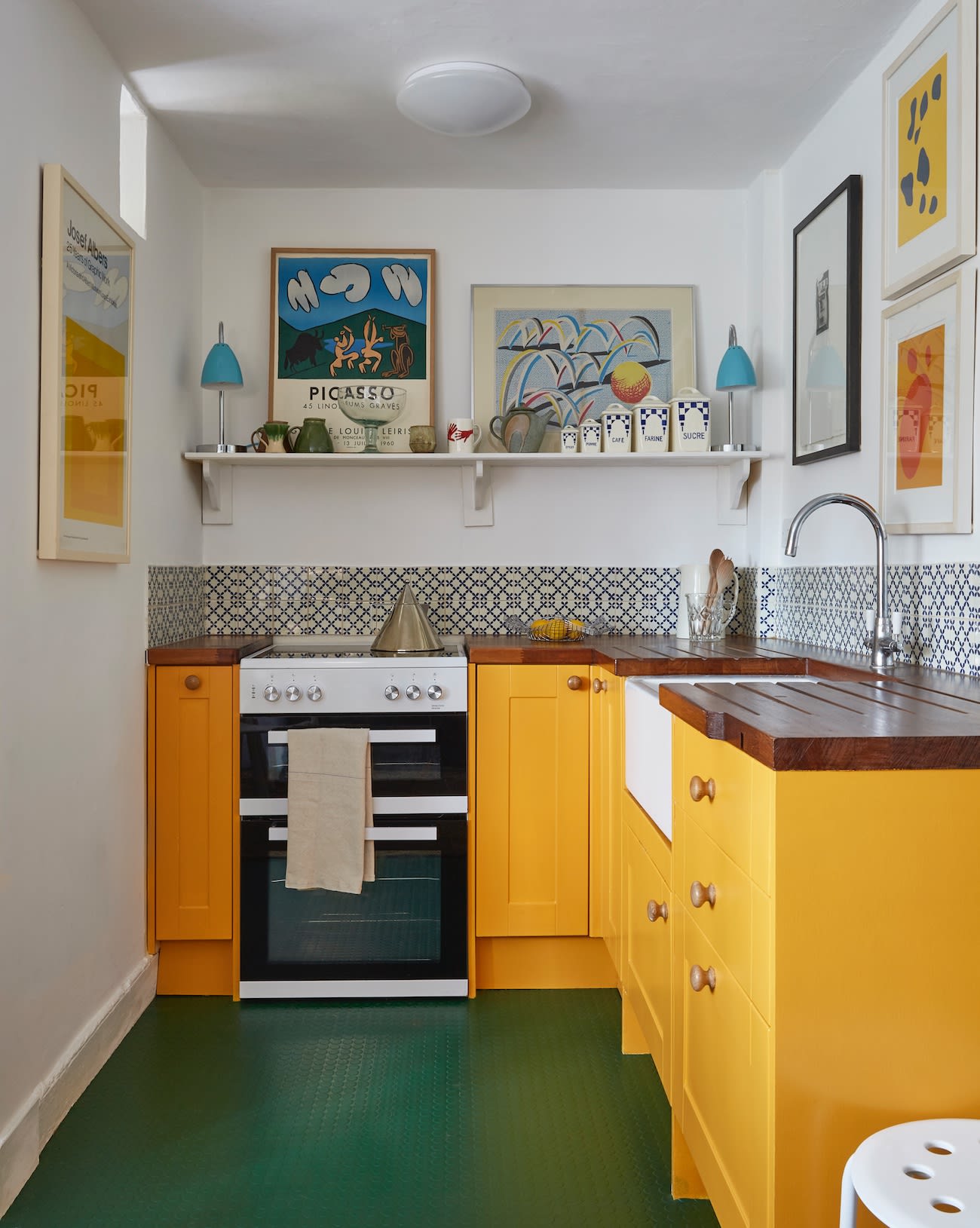 The dinky kitchen is spruced up with factory-worthy industrial flooring and gold-orange cabinets.